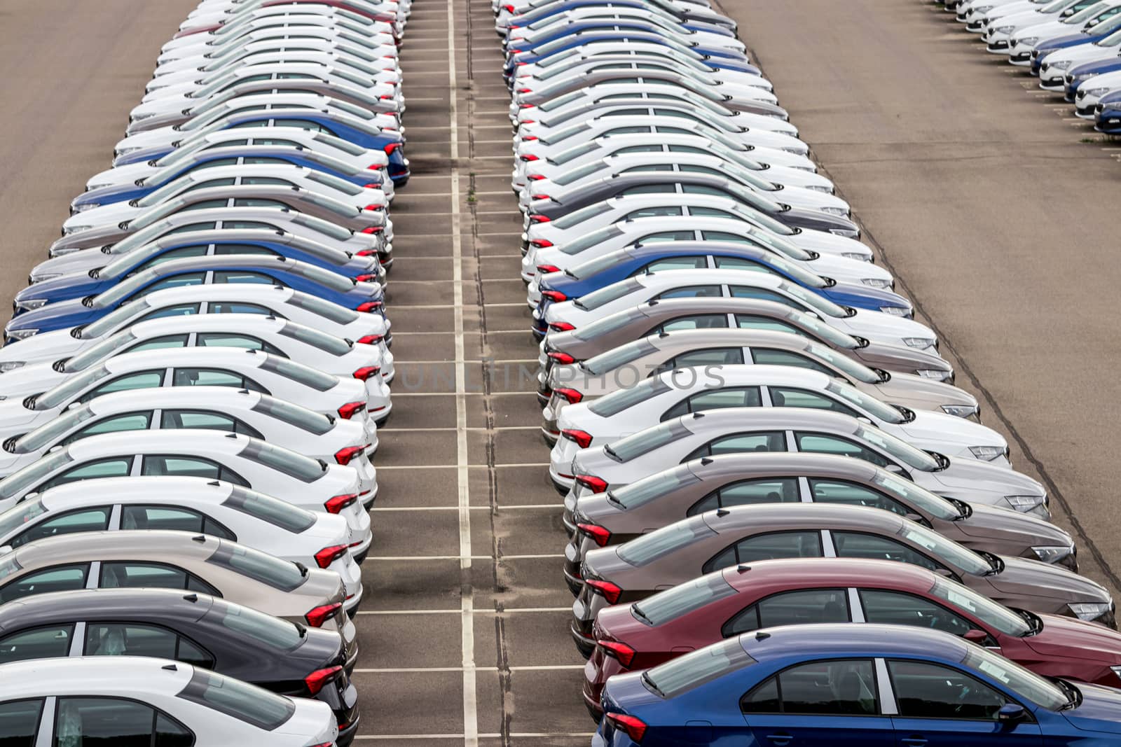 Rows of a new cars parked in a distribution center on a car factory on a cloudy day. Top view to the parking in the open air. by Eugene_Yemelyanov