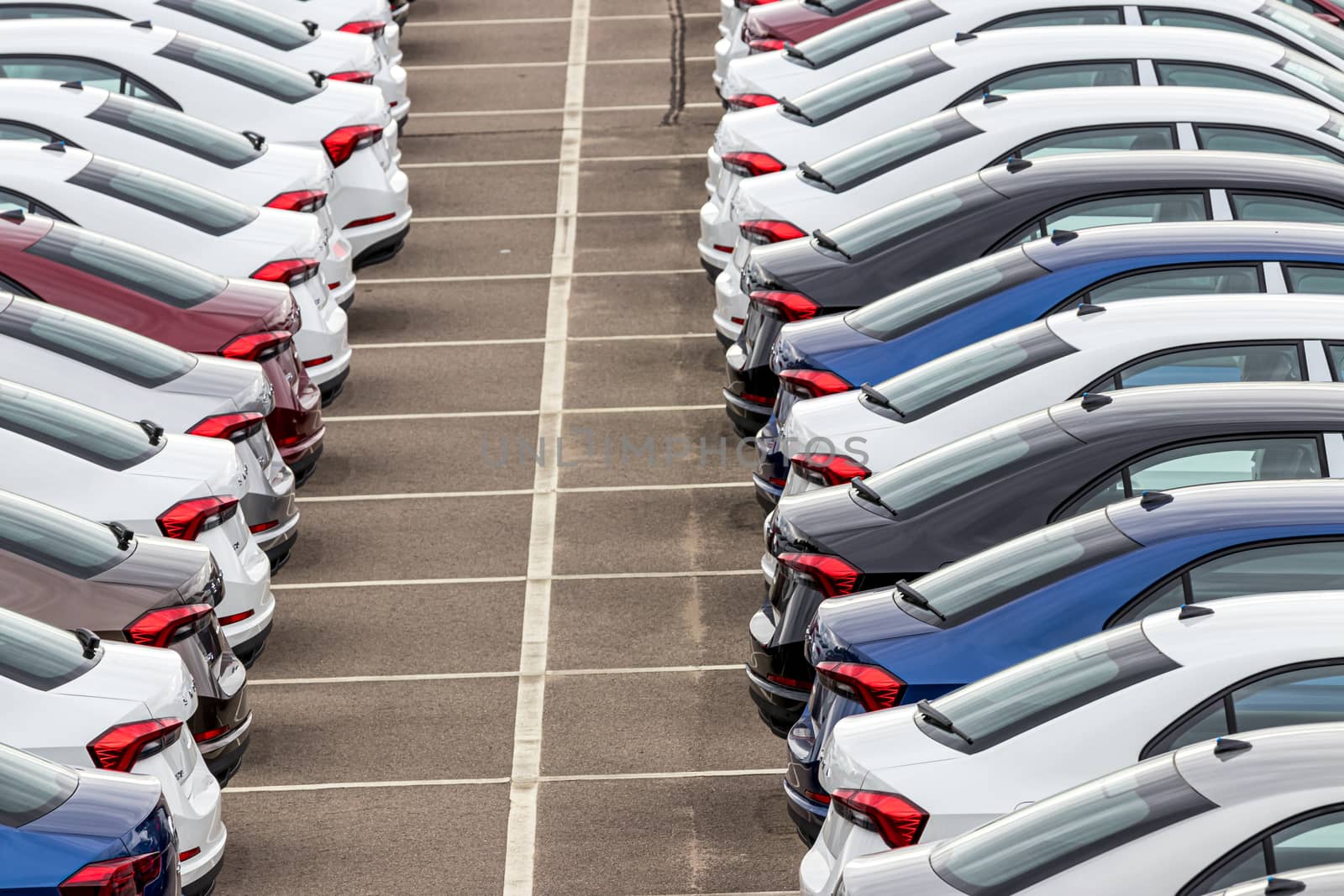 Rows of a new cars parked in a distribution center of a car factory. Top view to the parking in the open air.