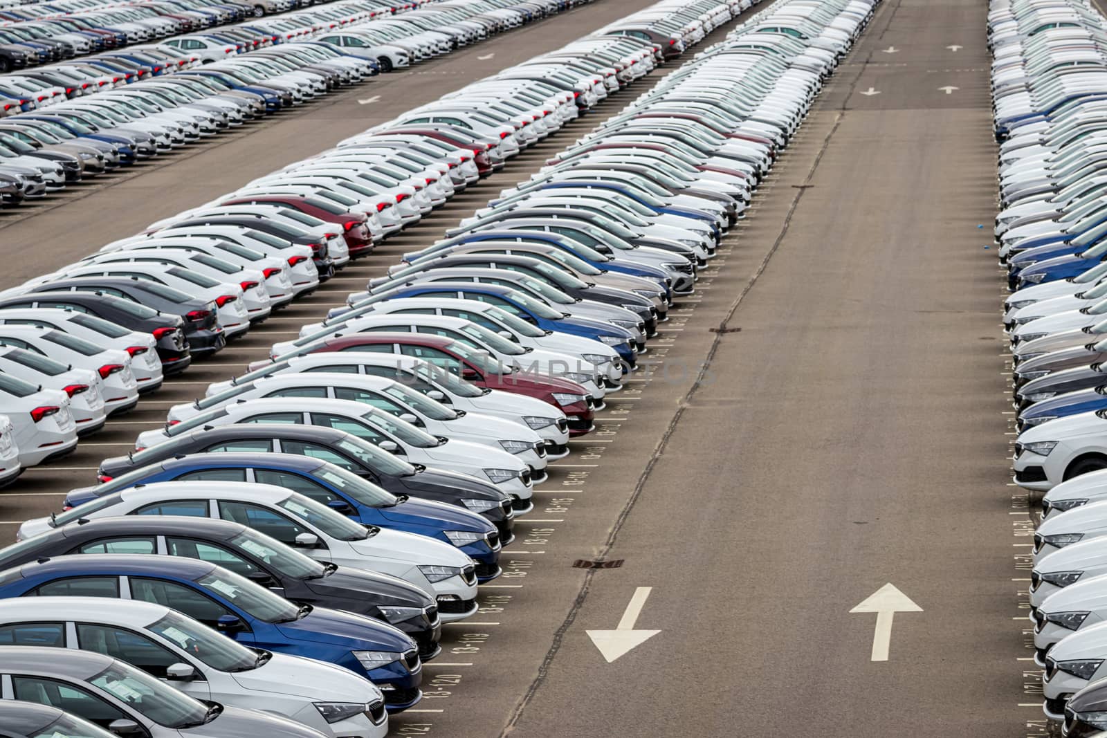 Rows of a new cars parked in a distribution center on a cloudy day in the spring, a car factory. Top view to the parking in the open air.