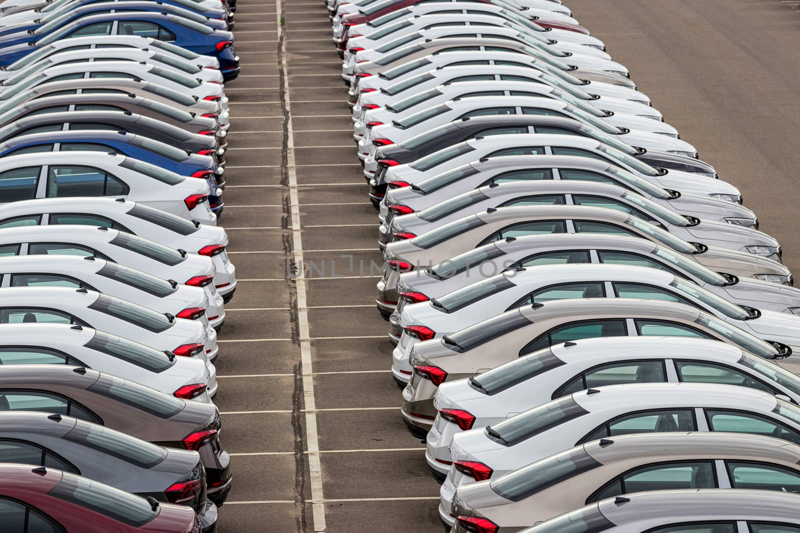 Rows of a new cars parked in a distribution center on a cloudy day in the spring, a car factory. Top view to the parking in the open air. by Eugene_Yemelyanov