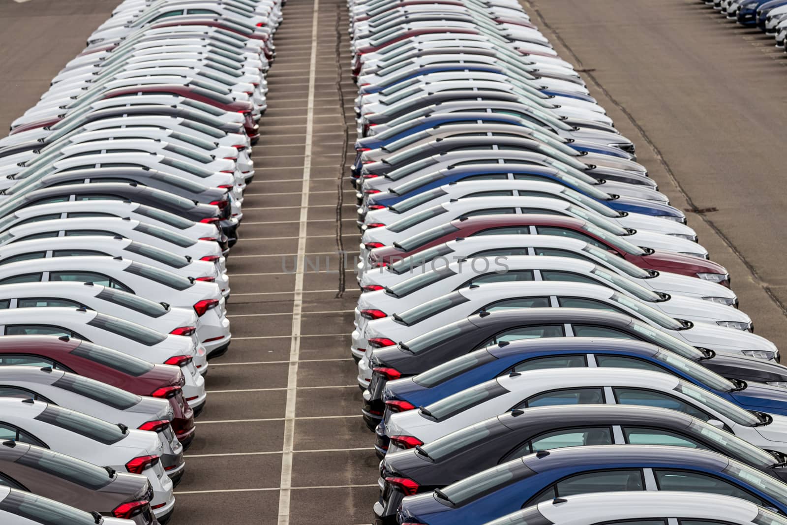 Rows of a new cars parked in a distribution center on a cloudy day in the spring, a car factory. Top view to the parking in the open air. by Eugene_Yemelyanov