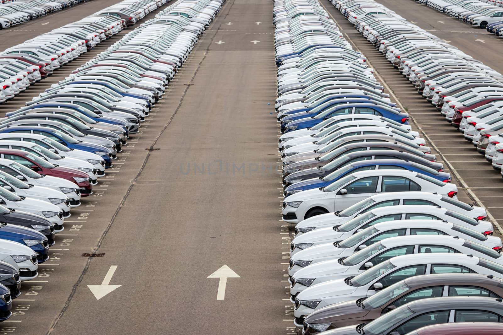 Rows of a new cars parked in a distribution center on a car factory on a cloudy day. Top view to the parking in the open air. by Eugene_Yemelyanov