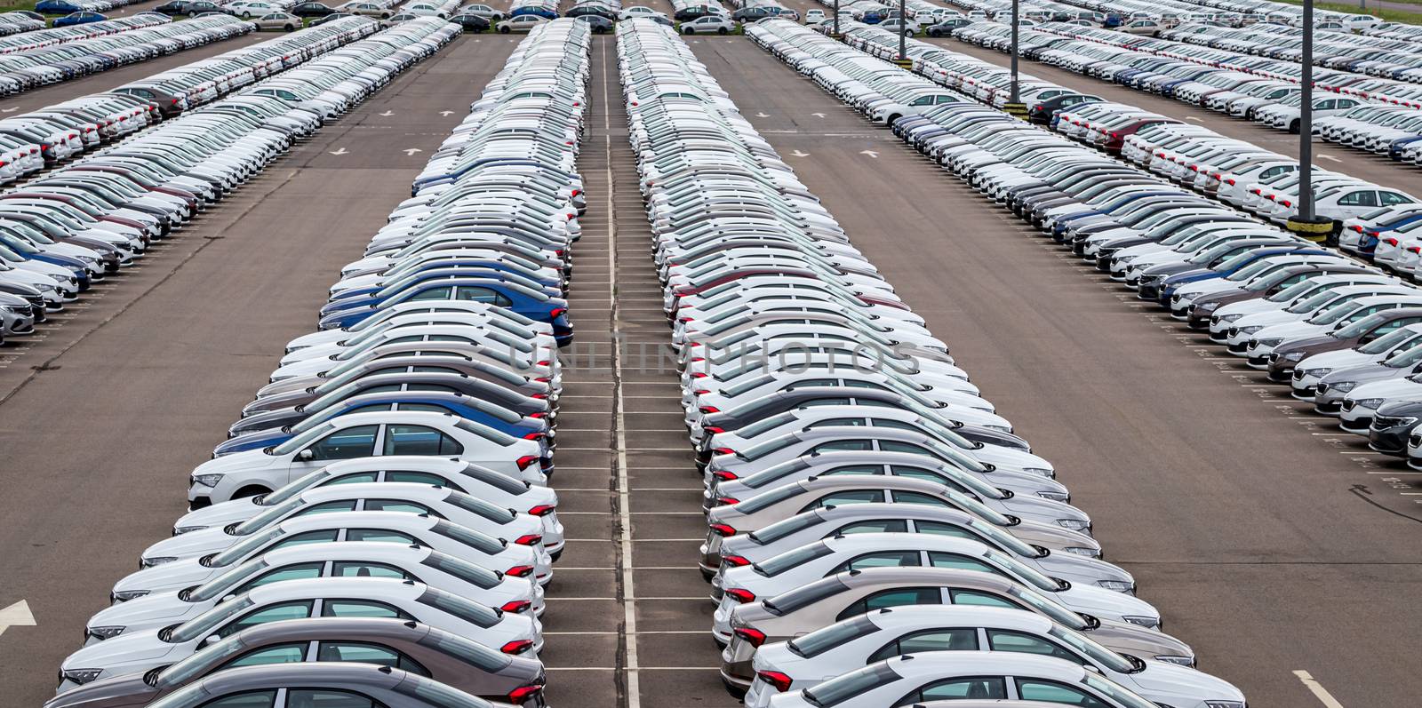 Rows of a new cars parked in a distribution center on a car factory on a cloudy day. Top view to the parking in the open air. by Eugene_Yemelyanov