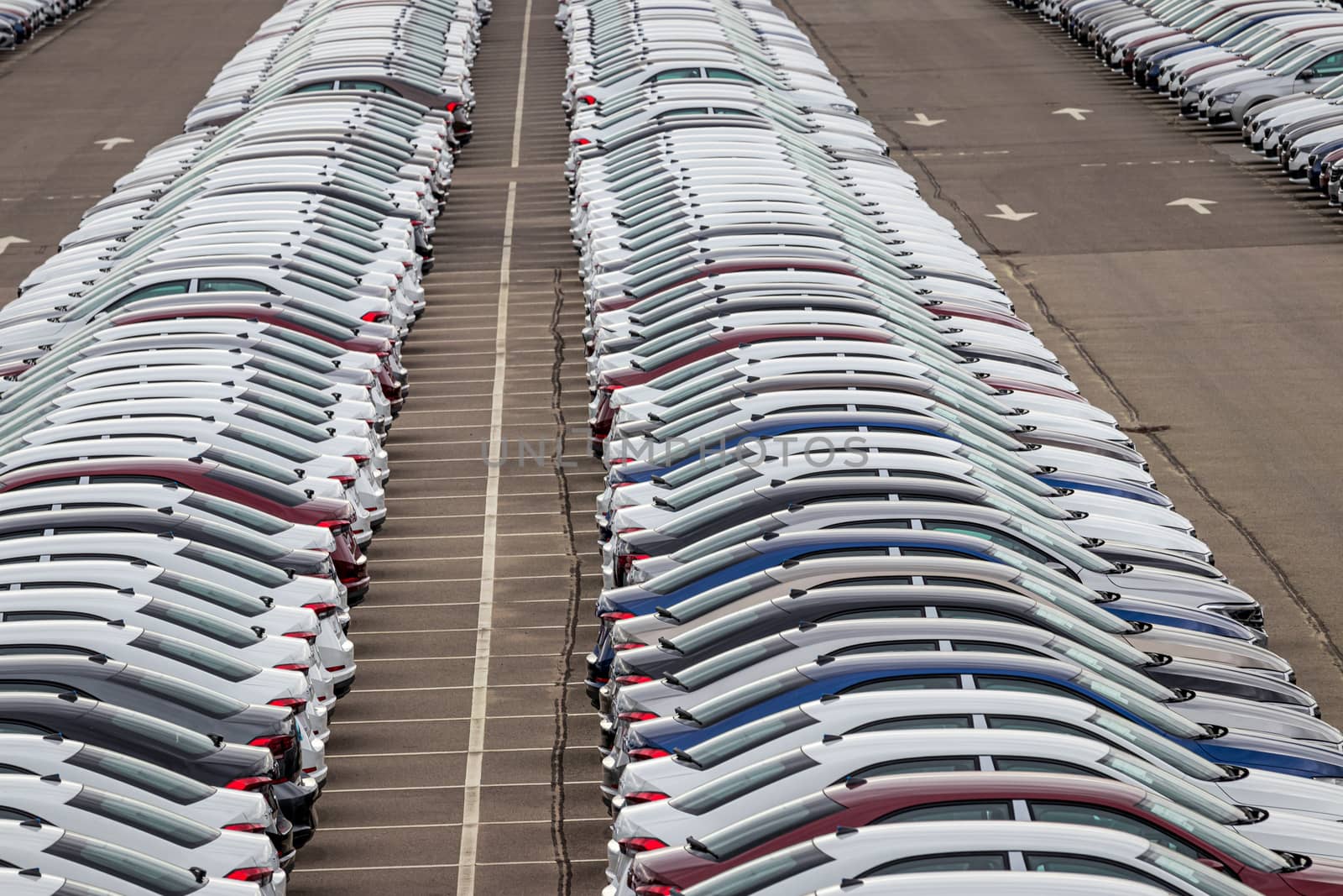 Rows of a new cars parked in a distribution center on a car factory on a cloudy day. Top view to the parking in the open air.