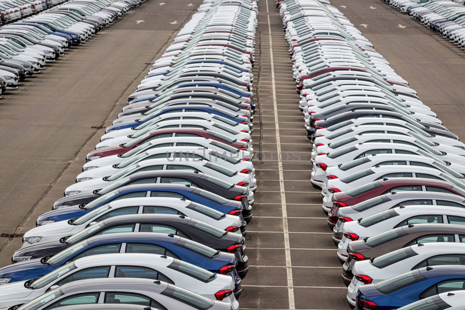 Rows of a new cars parked in a distribution center on a car factory on a cloudy day. Top view to the parking in the open air. by Eugene_Yemelyanov