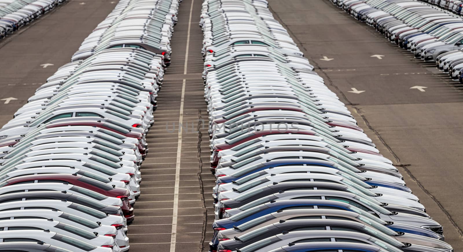 Rows of a new cars parked in a distribution center of a car factory. Top view to the parking in the open air.