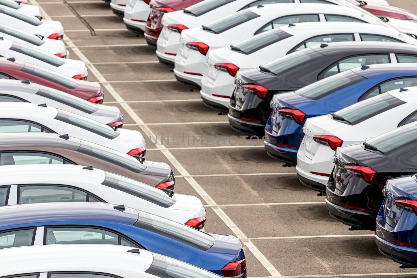 Rows of a new cars parked in a distribution center on a car factory on a cloudy day. Top view to the parking in the open air. by Eugene_Yemelyanov