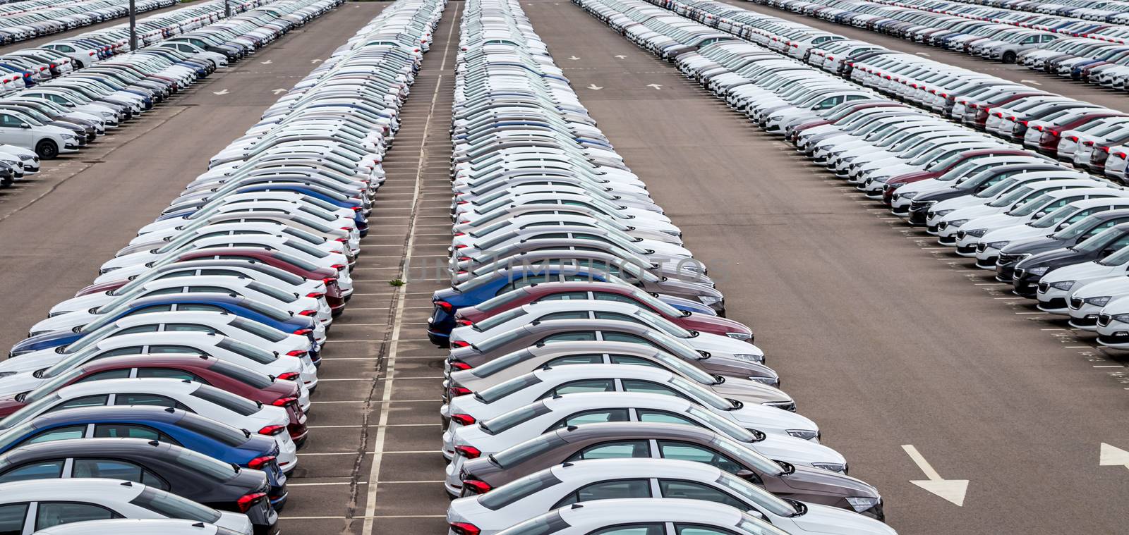 Rows of a new cars parked in a distribution center on a car factory on a cloudy day. Top view to the parking in the open air. by Eugene_Yemelyanov