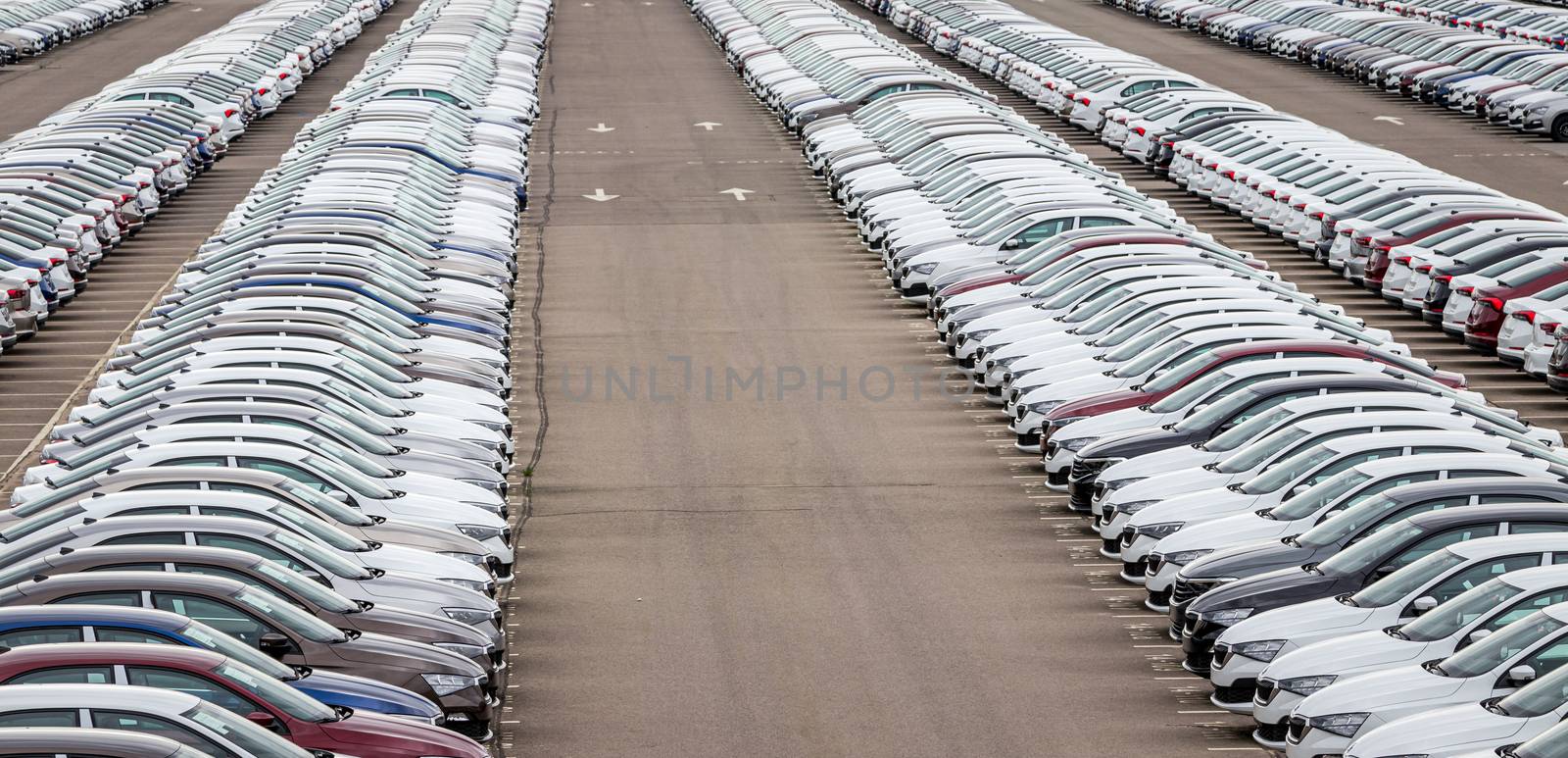 Rows of a new cars parked in a distribution center on a cloudy day in the spring, a car factory. Top view to the parking in the open air. by Eugene_Yemelyanov