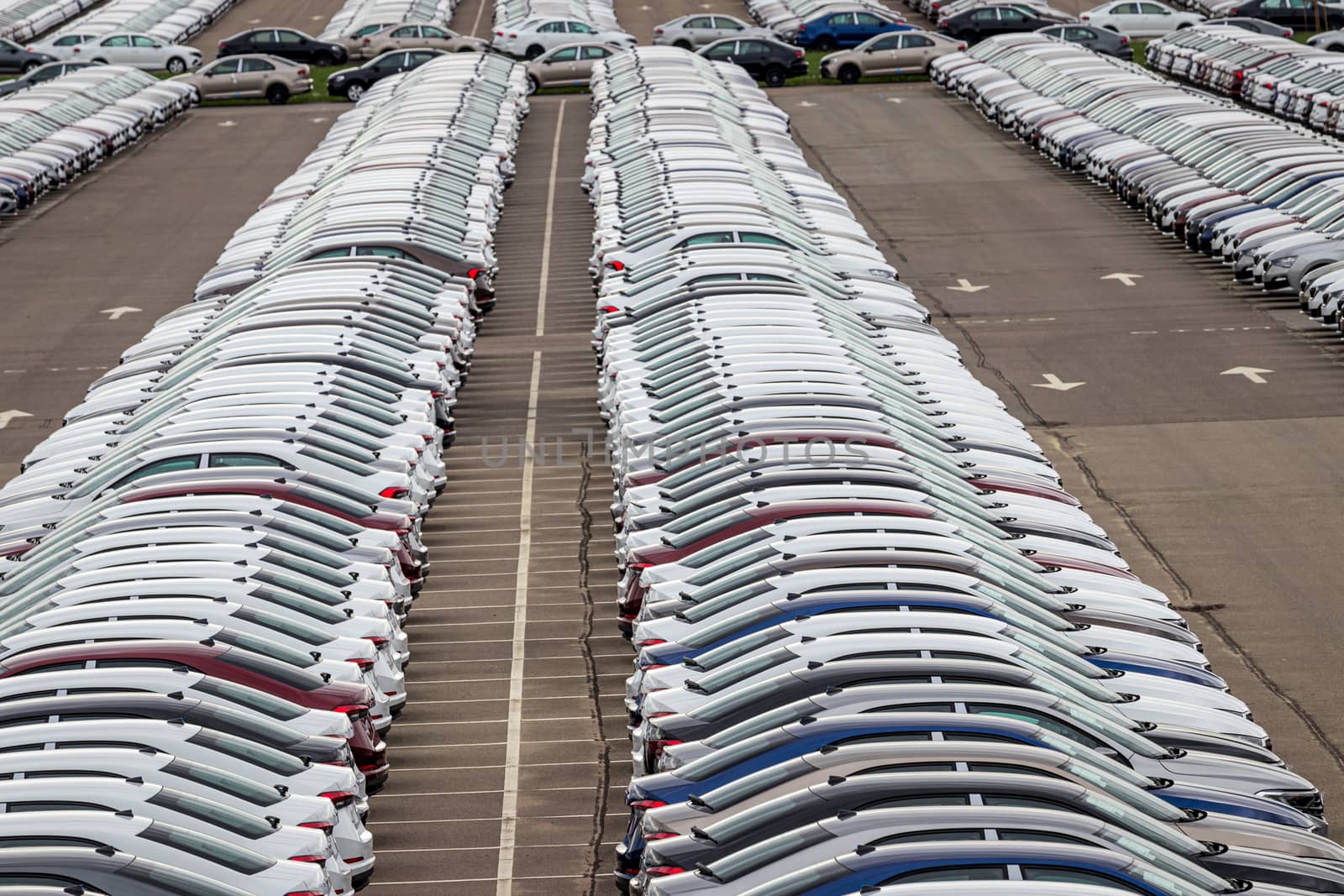 Rows of a new cars parked in a distribution center on a cloudy day in the spring, a car factory. Top view to the parking in the open air. by Eugene_Yemelyanov