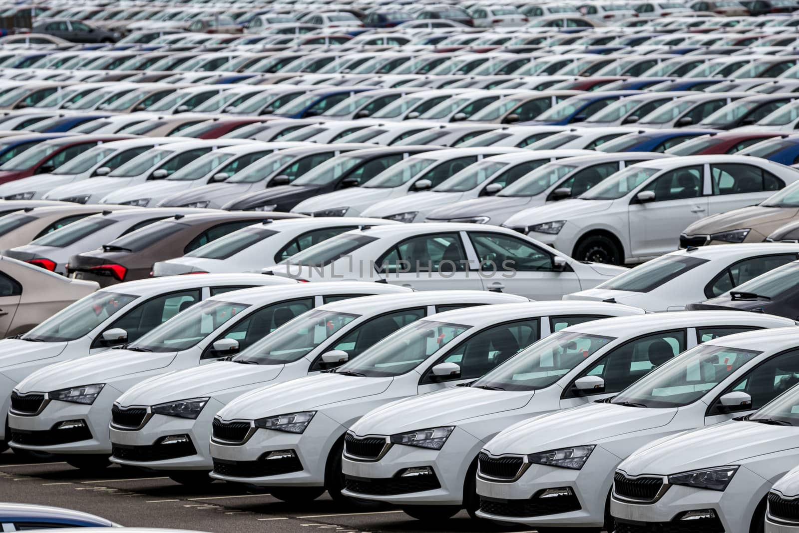 Rows of a new cars parked in a distribution center of a car factory. Top view to the parking in the open air.