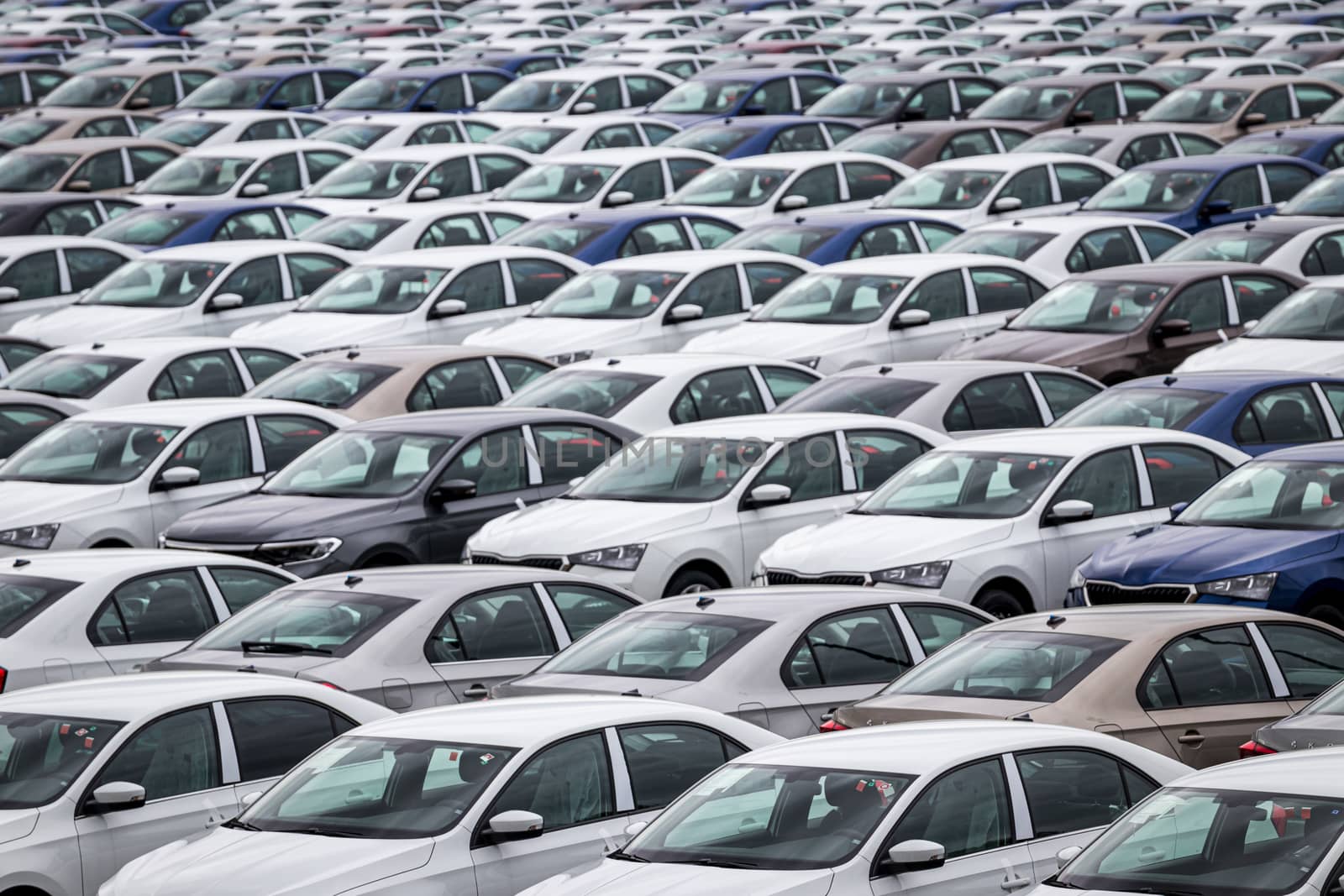 Rows of a new cars parked in a distribution center of a car factory. Top view to the parking in the open air. by Eugene_Yemelyanov