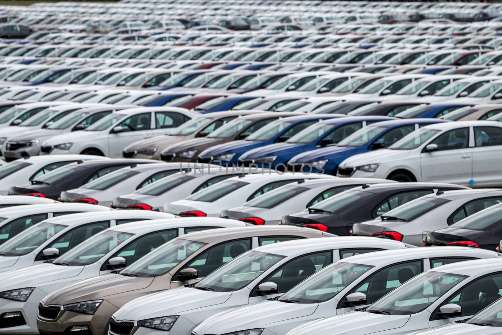 Rows of a new cars parked in a distribution center on a cloudy day in the spring, a car factory. Top view to the parking in the open air.