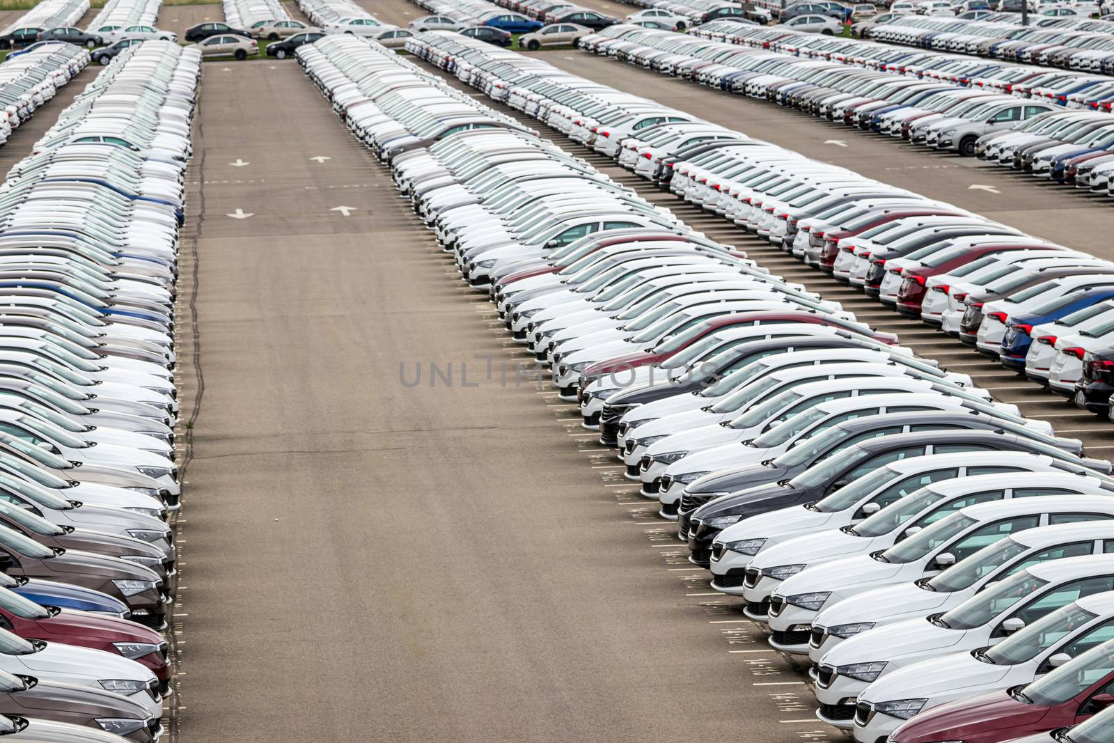 Rows of a new cars parked in a distribution center on a car factory on a cloudy day. Top view to the parking in the open air. by Eugene_Yemelyanov