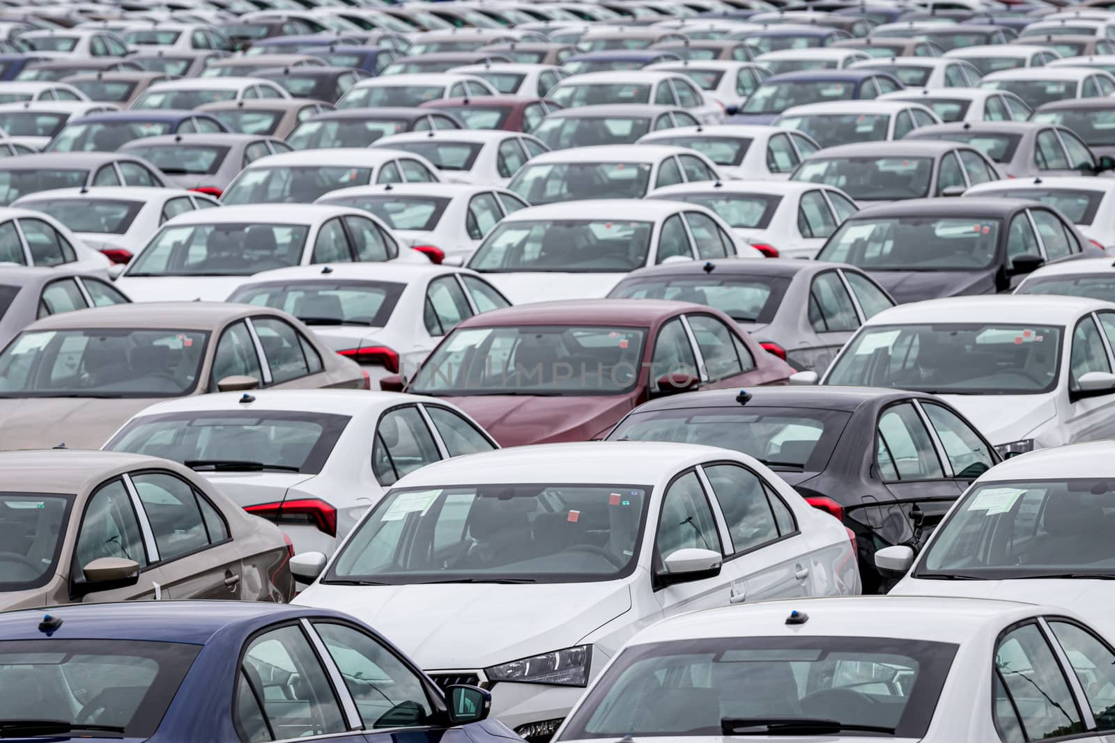 Rows of a new cars parked in a distribution center on a cloudy day in the spring, a car factory. Top view to the parking in the open air.