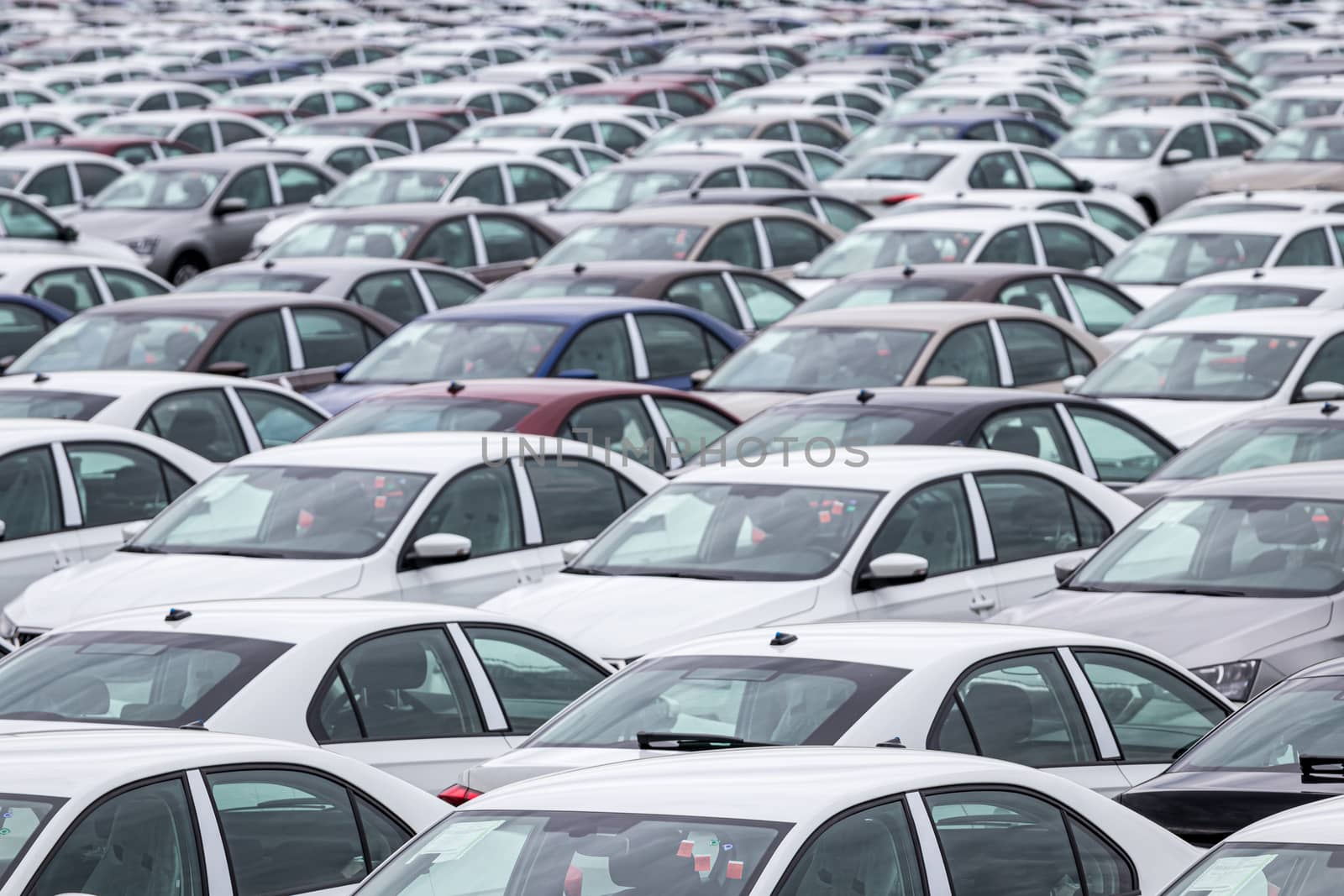 Rows of a new cars parked in a distribution center of a car factory. Top view to the parking in the open air.