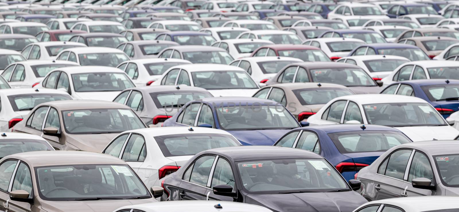 Rows of a new cars parked in a distribution center of a car factory. Top view to the parking in the open air.