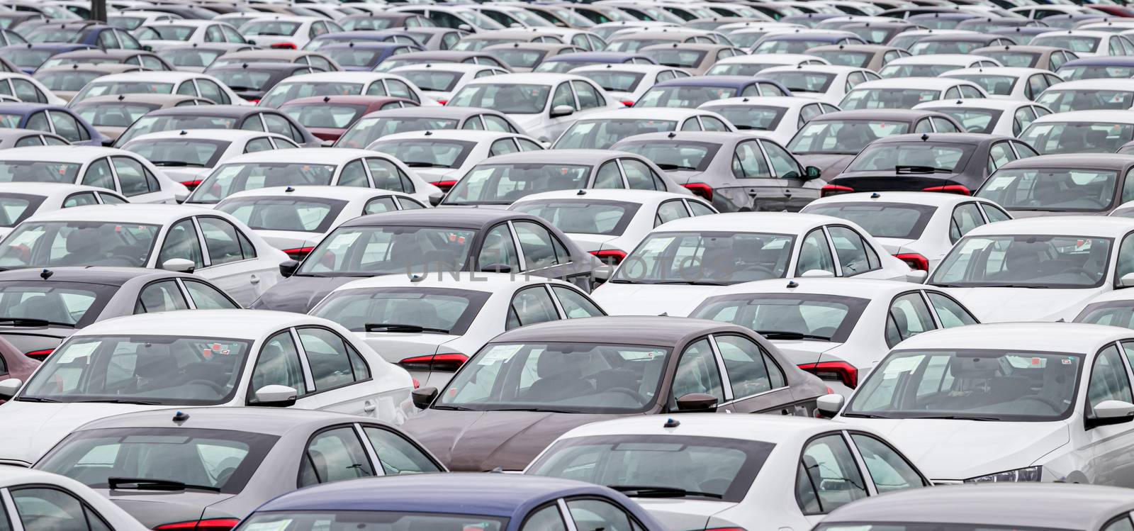 Rows of a new cars parked in a distribution center on a cloudy day in the spring, a car factory. Top view to the parking in the open air.