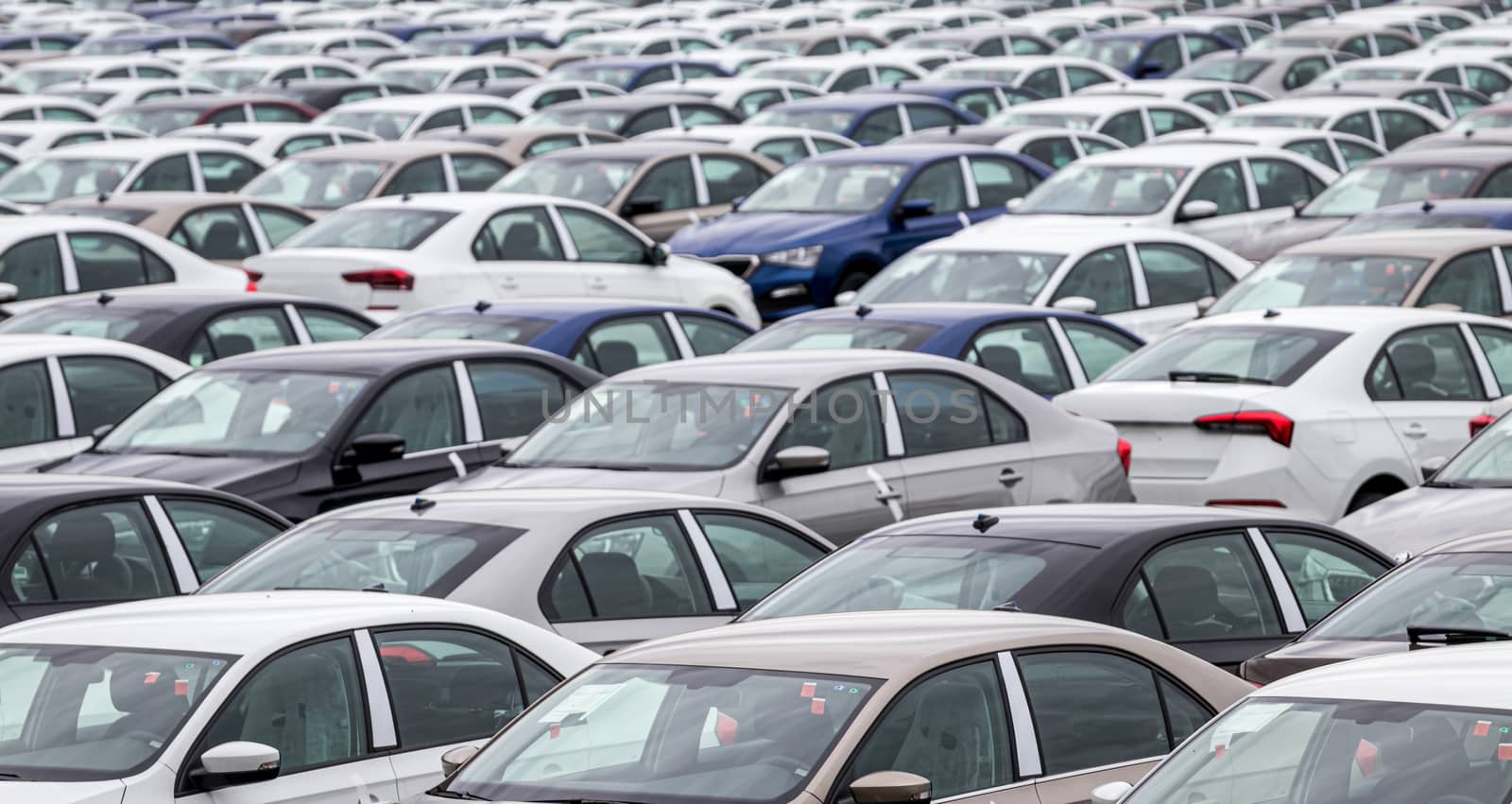 Rows of a new cars parked in a distribution center on a cloudy day in the spring, a car factory. Top view to the parking in the open air. by Eugene_Yemelyanov