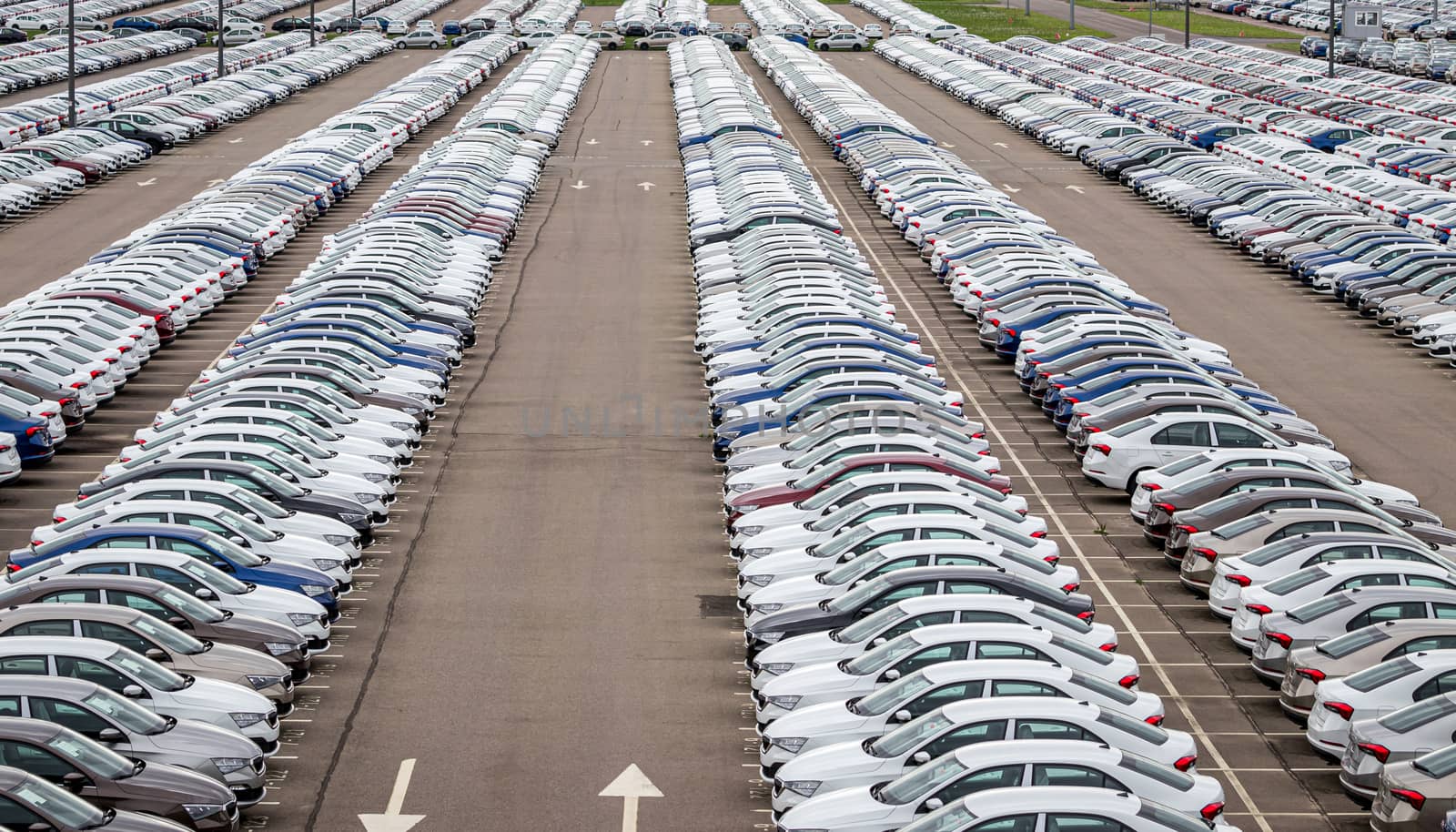 Rows of a new cars parked in a distribution center on a cloudy day in the spring, a car factory. Top view to the parking in the open air. by Eugene_Yemelyanov