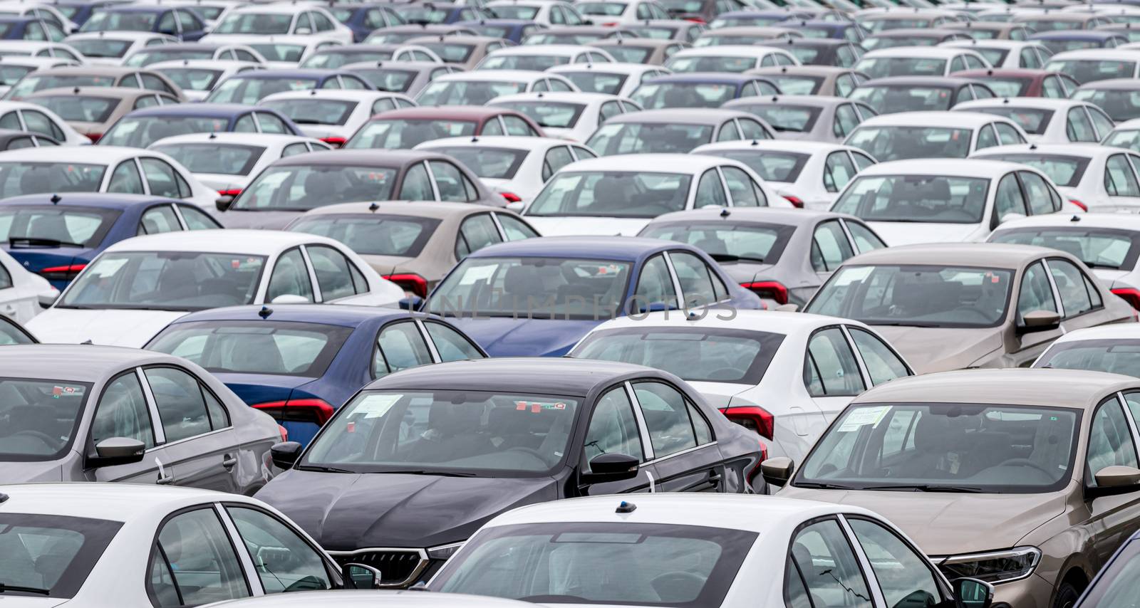 Rows of a new cars parked in a distribution center on a car factory on a cloudy day. Top view to the parking in the open air. by Eugene_Yemelyanov