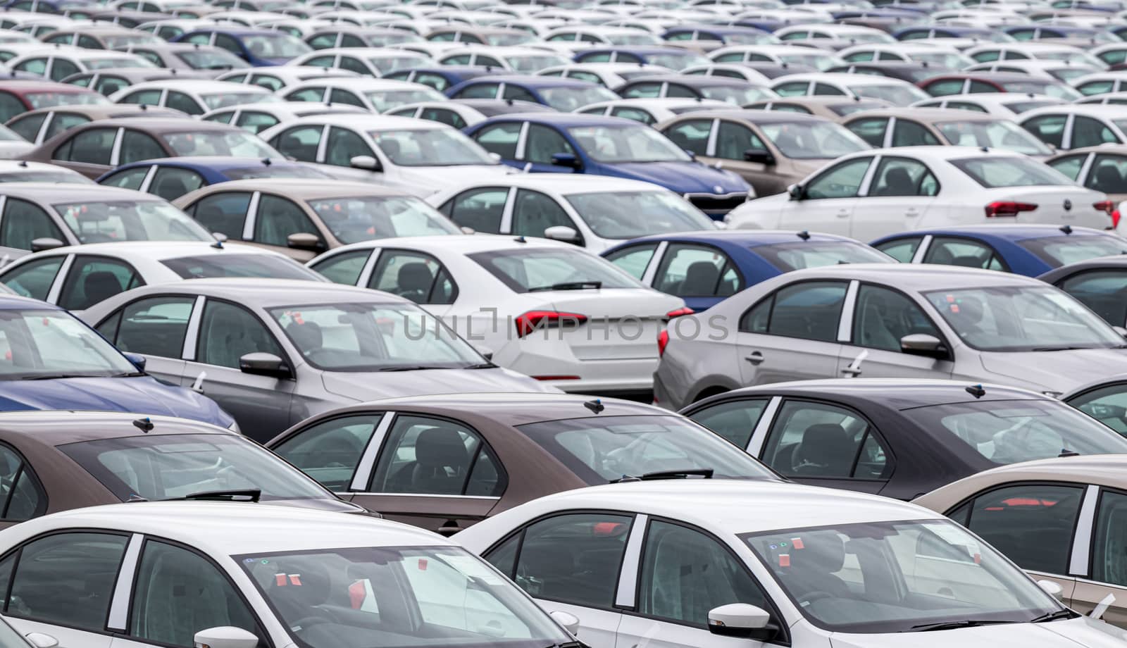 Rows of a new cars parked in a distribution center of a car factory. Top view to the parking in the open air. by Eugene_Yemelyanov