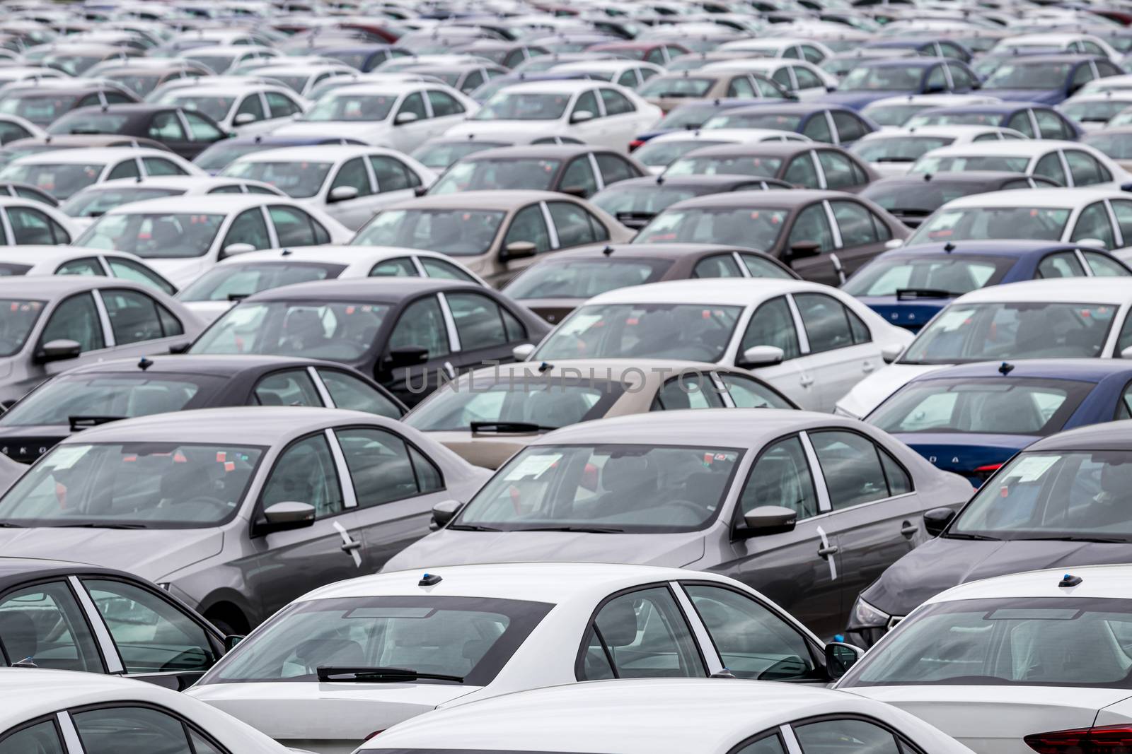 Rows of a new cars parked in a distribution center on a car factory on a cloudy day. Top view to the parking in the open air. by Eugene_Yemelyanov