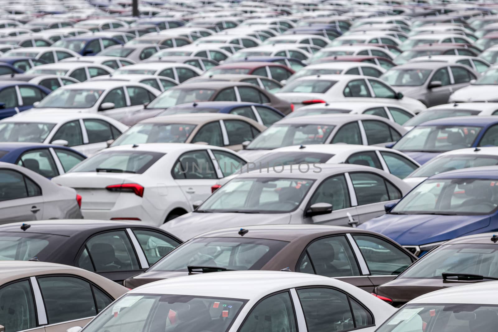 Rows of a new cars parked in a distribution center on a cloudy day in the spring, a car factory. Top view to the parking in the open air.