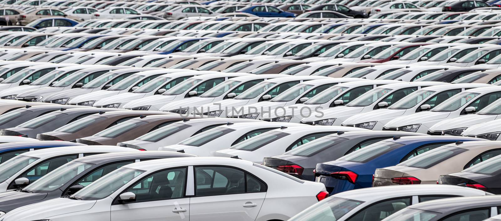 Rows of a new cars parked in a distribution center on a car factory on a cloudy day. Top view to the parking in the open air. by Eugene_Yemelyanov