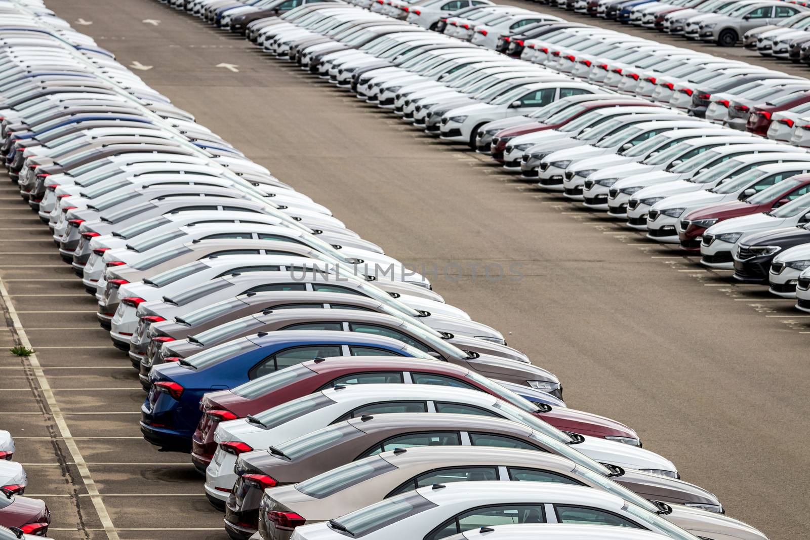 Rows of a new cars parked in a distribution center on a car factory on a cloudy day. Top view to the parking in the open air. by Eugene_Yemelyanov