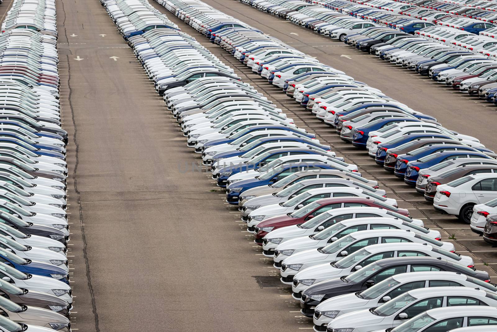 Rows of a new cars parked in a distribution center on a car factory on a cloudy day. Top view to the parking in the open air. by Eugene_Yemelyanov