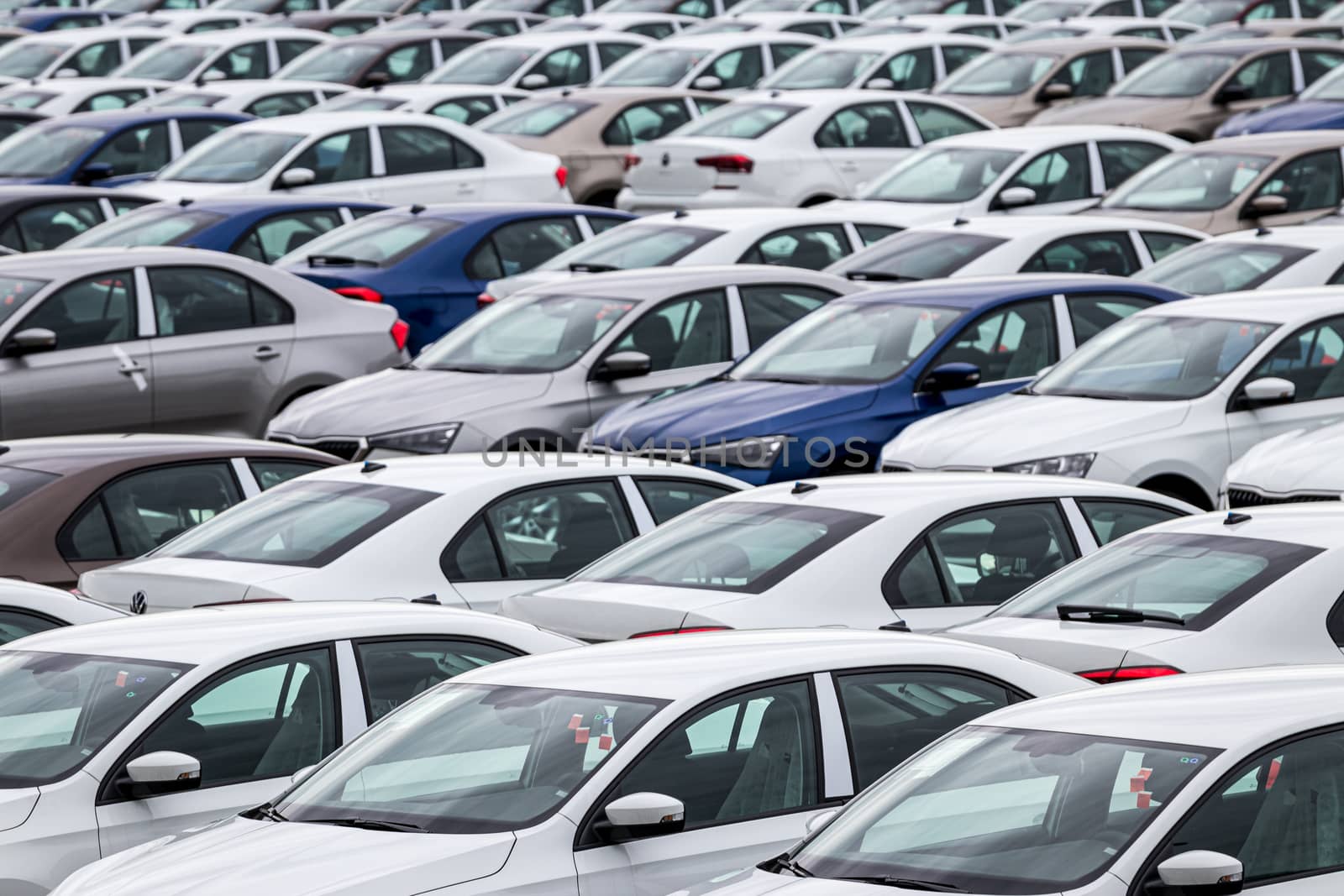 Rows of a new cars parked in a distribution center on a cloudy day in the spring, a car factory. Top view to the parking in the open air. by Eugene_Yemelyanov