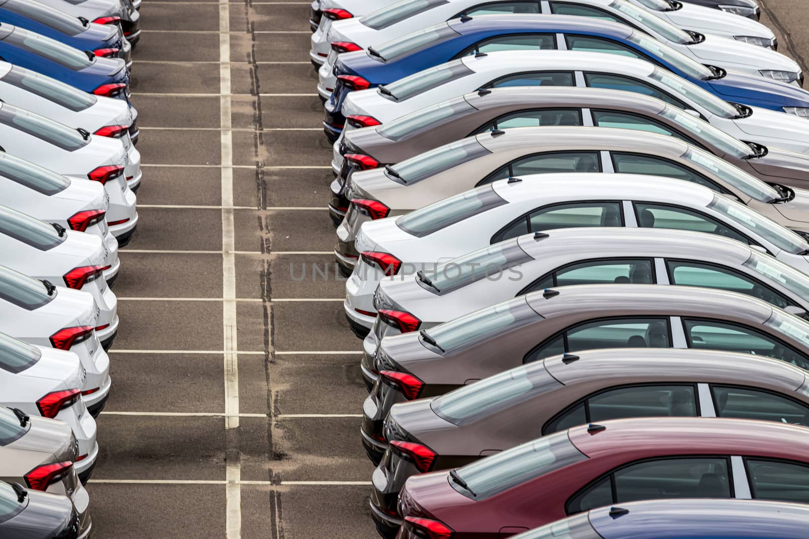 Rows of a new cars parked in a distribution center on a cloudy day in the spring, a car factory. Top view to the parking in the open air. by Eugene_Yemelyanov