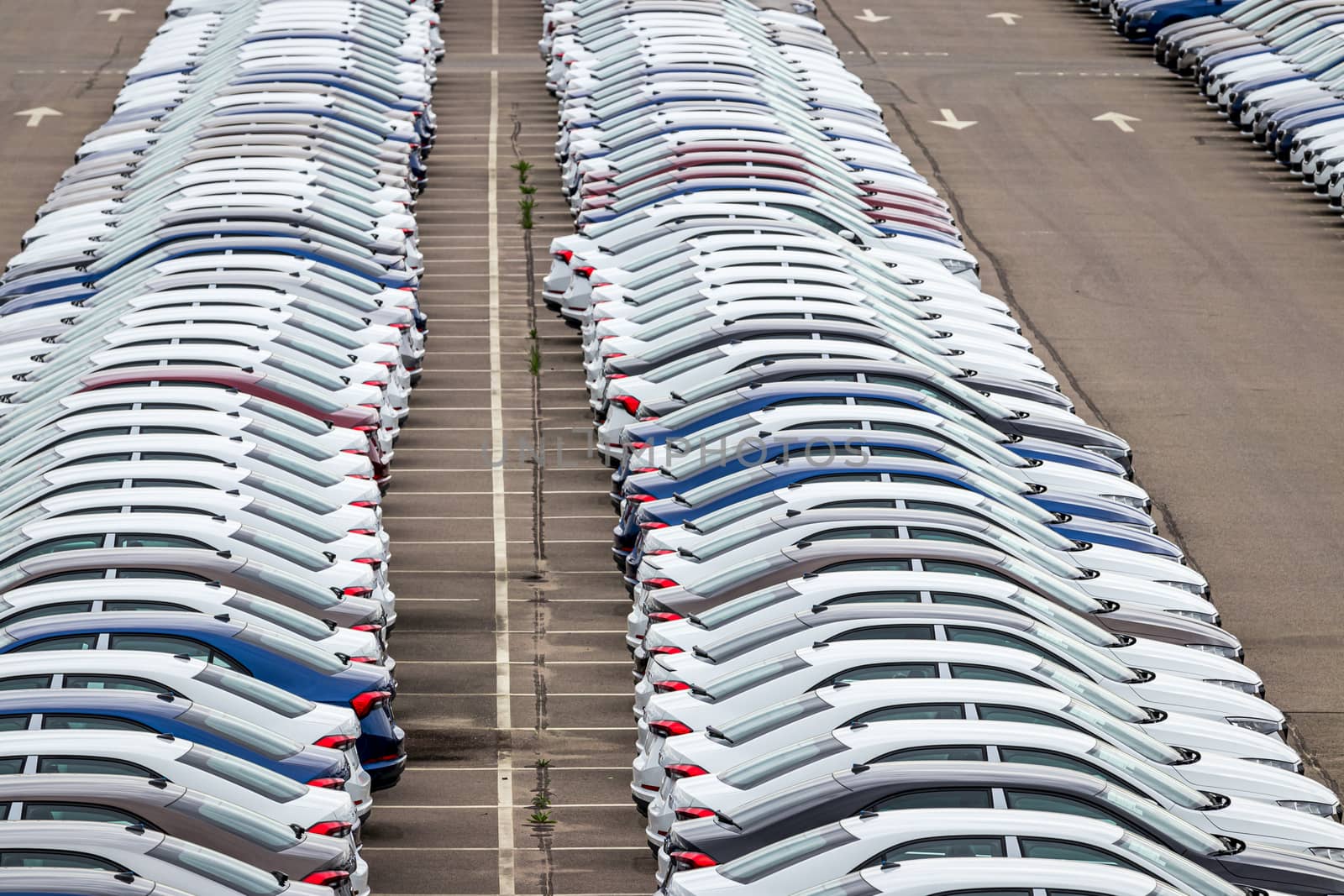 Rows of a new cars parked in a distribution center on a cloudy day in the spring, a car factory. Top view to the parking in the open air. by Eugene_Yemelyanov