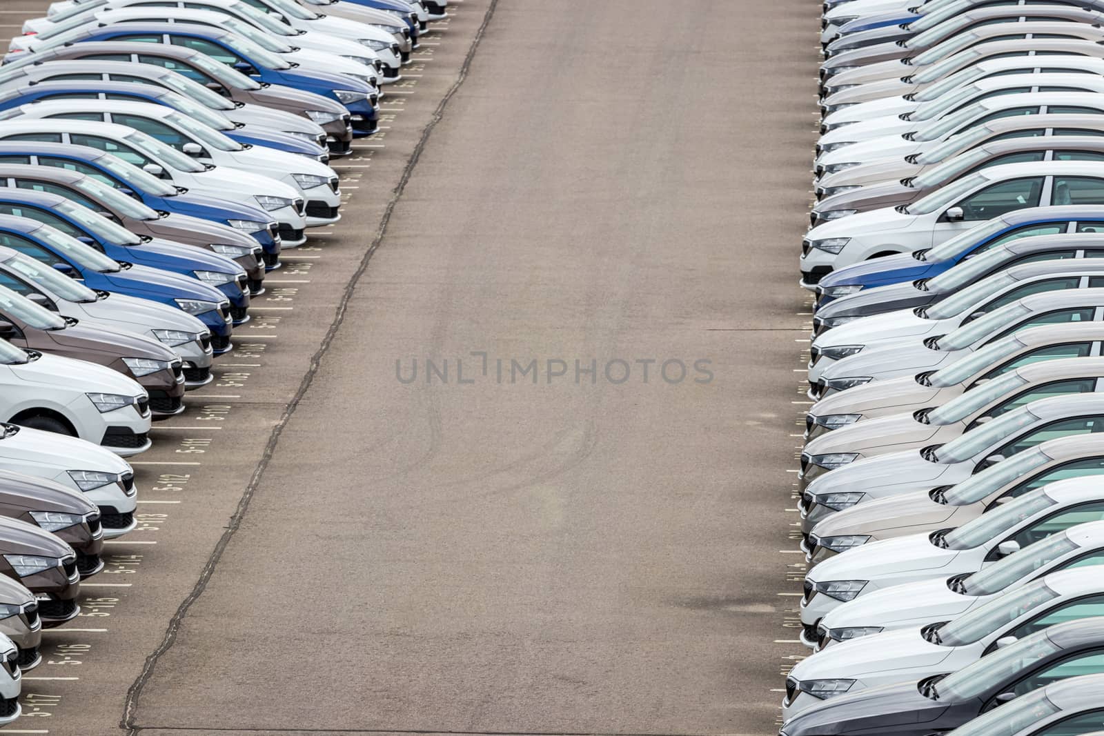 Rows of a new cars parked in a distribution center of a car factory. Top view to the parking in the open air.