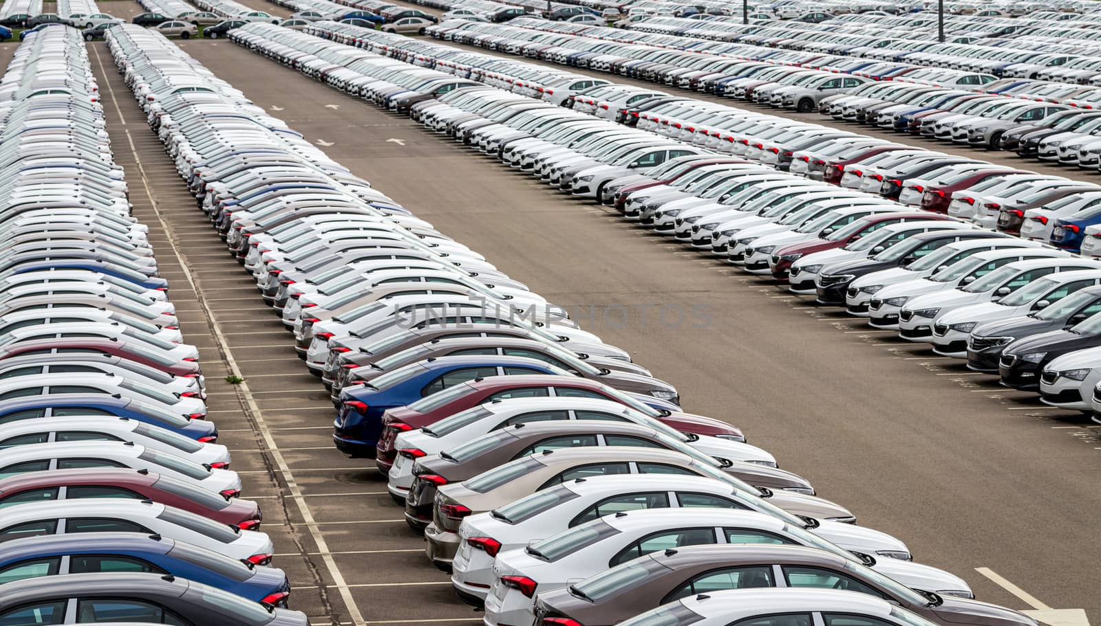 Rows of a new cars parked in a distribution center on a cloudy day in the spring, a car factory. Top view to the parking in the open air.