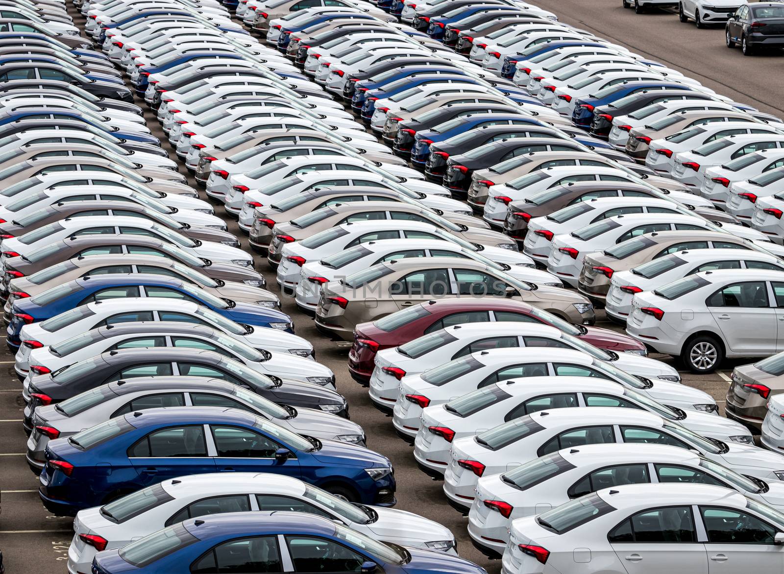 Rows of a new cars parked in a distribution center on a car factory on a cloudy day. Top view to the parking in the open air.