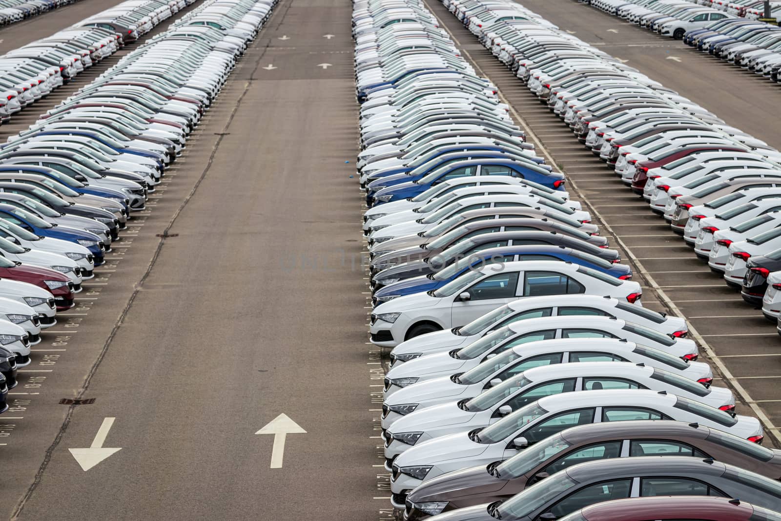 Rows of a new cars parked in a distribution center of a car factory. Top view to the parking in the open air.