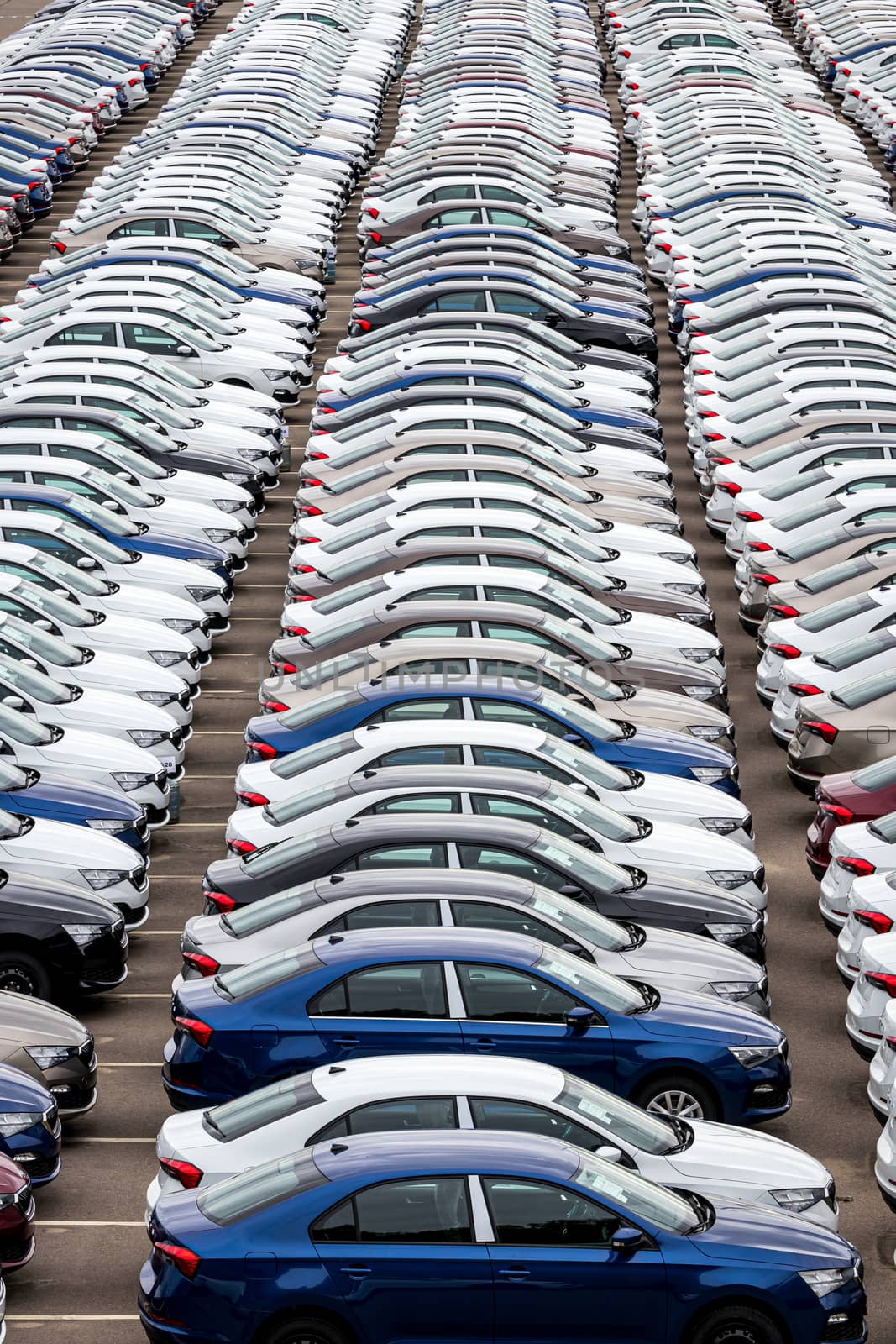 Rows of a new cars parked in a distribution center on a cloudy day in the spring, a car factory. Top view to the parking in the open air.