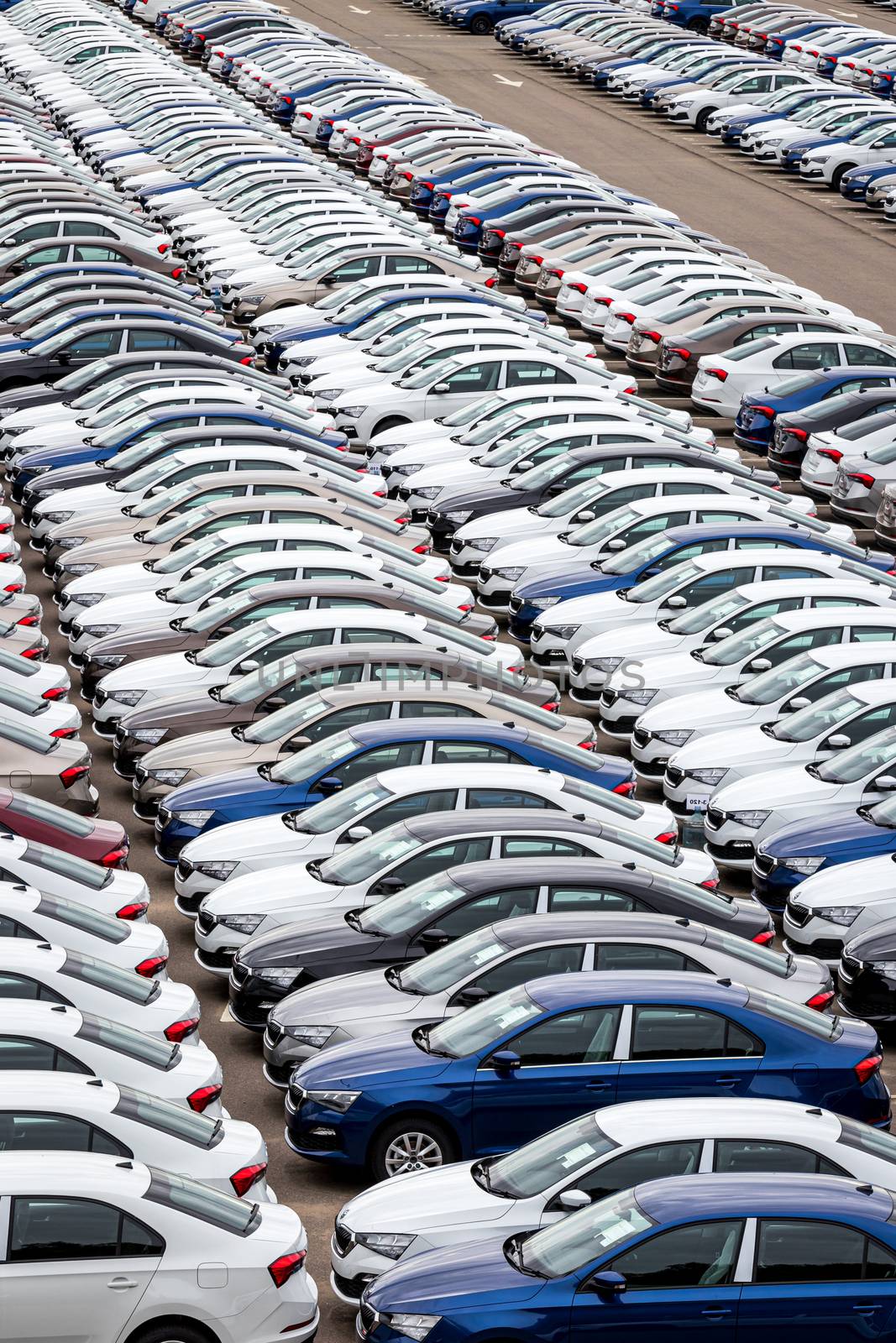 Rows of a new cars parked in a distribution center on a car factory on a cloudy day. Top view to the parking in the open air.