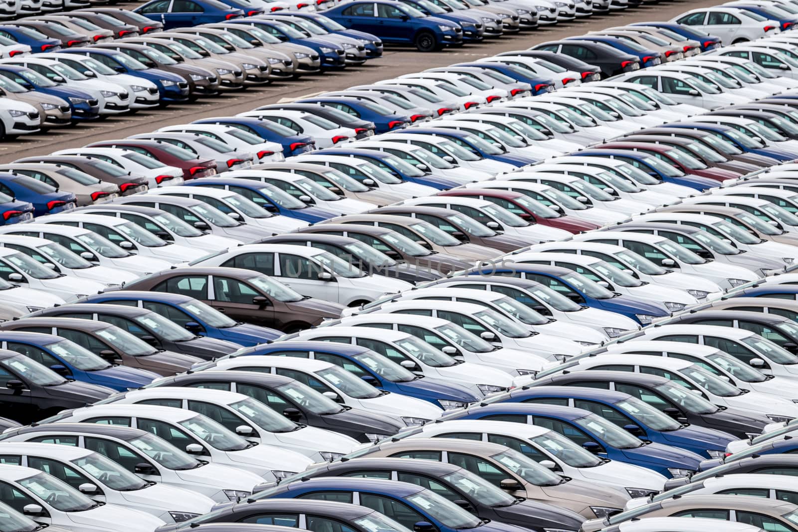 Rows of a new cars parked in a distribution center of a car factory. Top view to the parking in the open air.