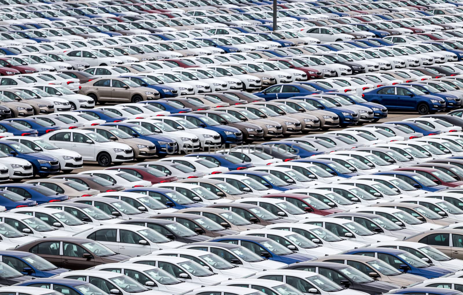 Rows of a new cars parked in a distribution center on a cloudy day in the spring, a car factory. Top view to the parking in the open air.