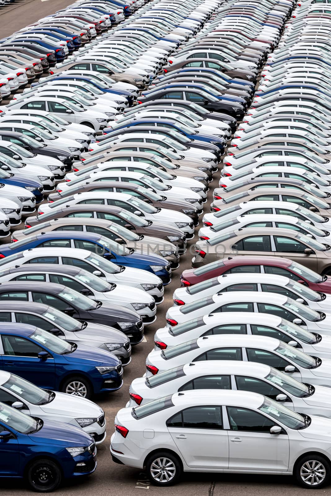 Rows of a new cars parked in a distribution center of a car factory. Top view to the parking in the open air.