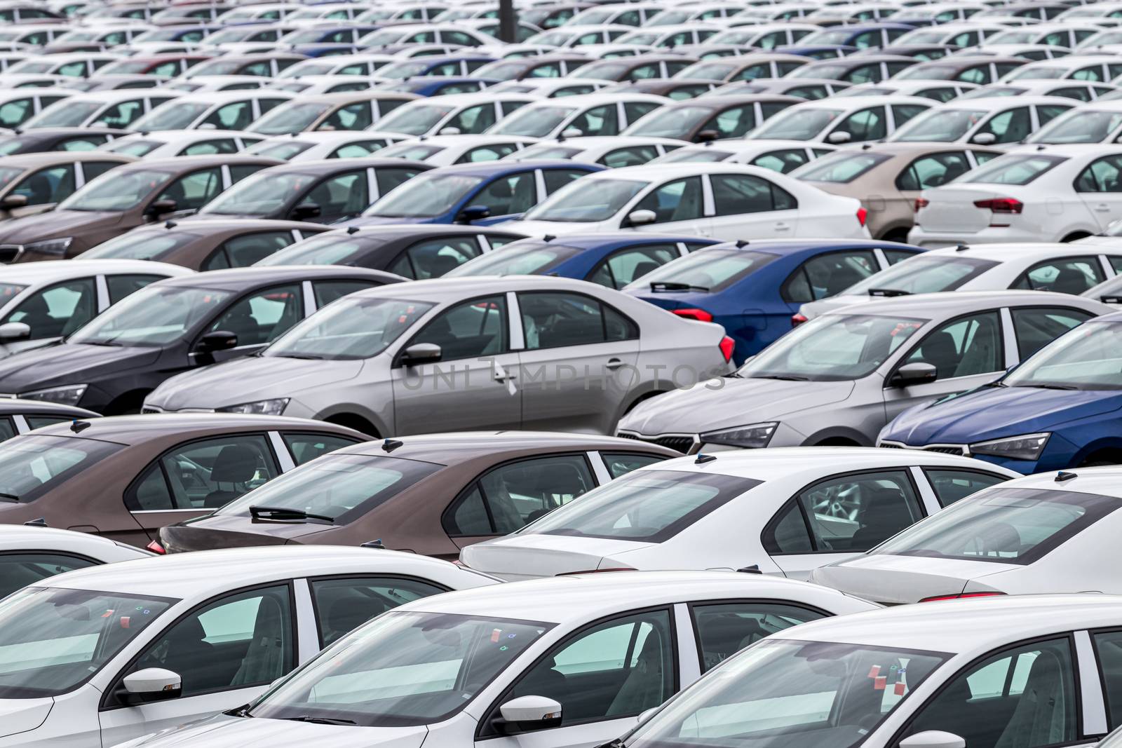 Rows of a new cars parked in a distribution center on a car factory on a cloudy day. Top view to the parking in the open air.