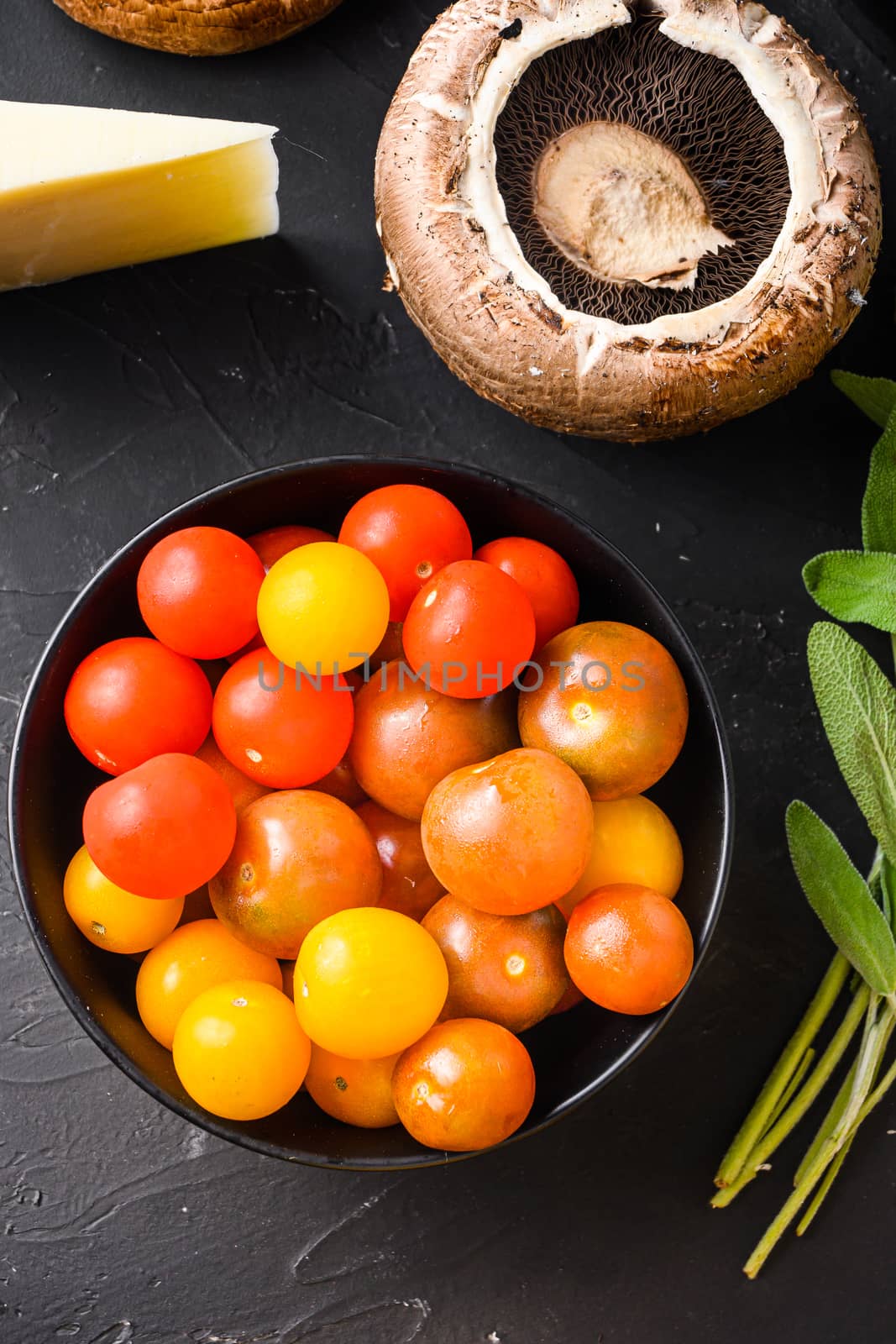 Cherry tomatoes in black bowl top view on black background