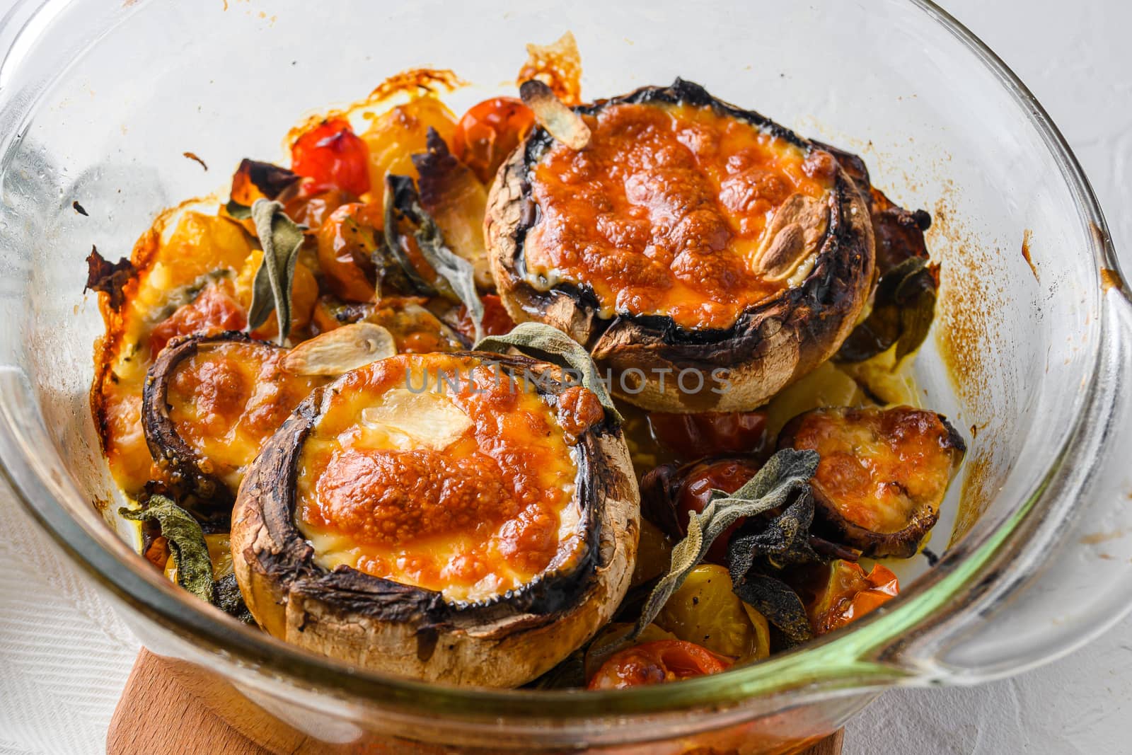 Portobello and ingredients for baking cheddar cheese, cherry tomatoes and sage in glass pot on white background side view close up selective focus