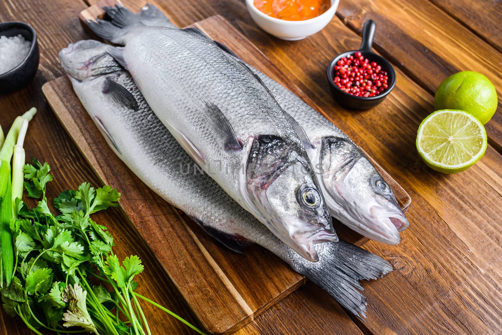 Couple sea bass with spices and herbs ingredients overwood table side view.