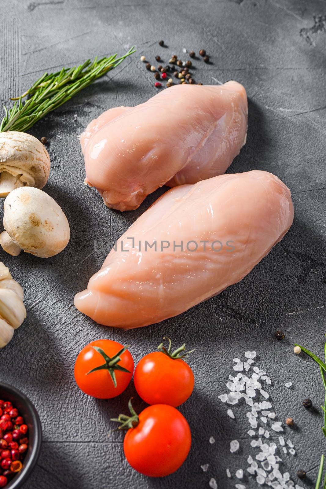 Raw chicken breast with fresh rosemary garlic, pepper and mushrooms on a grey concrete background side view. by Ilianesolenyi