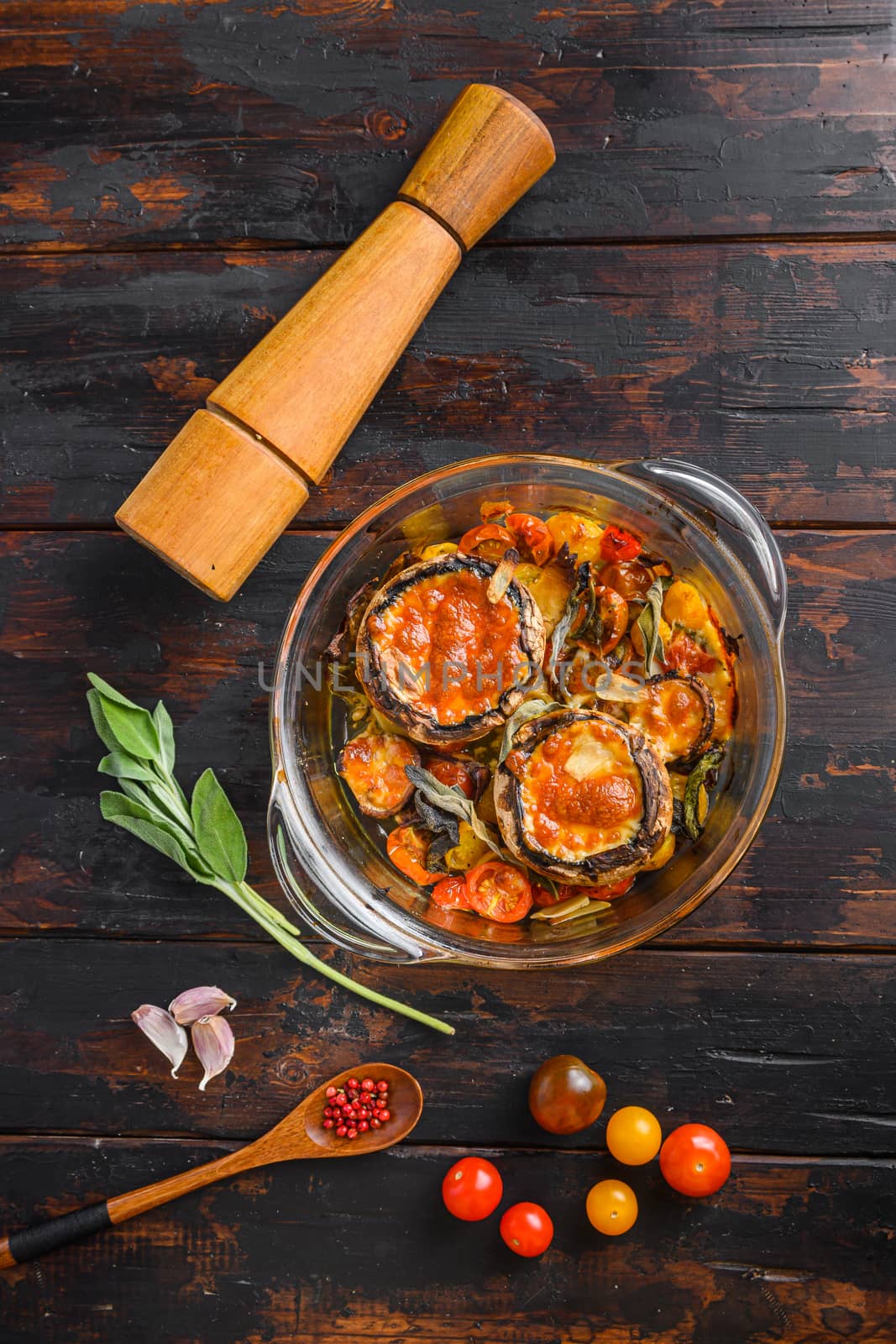 Portobello mushrooms,baked with cheddar cheese, cherry tomatoes and sage in glass pot on old wooden background top view. by Ilianesolenyi