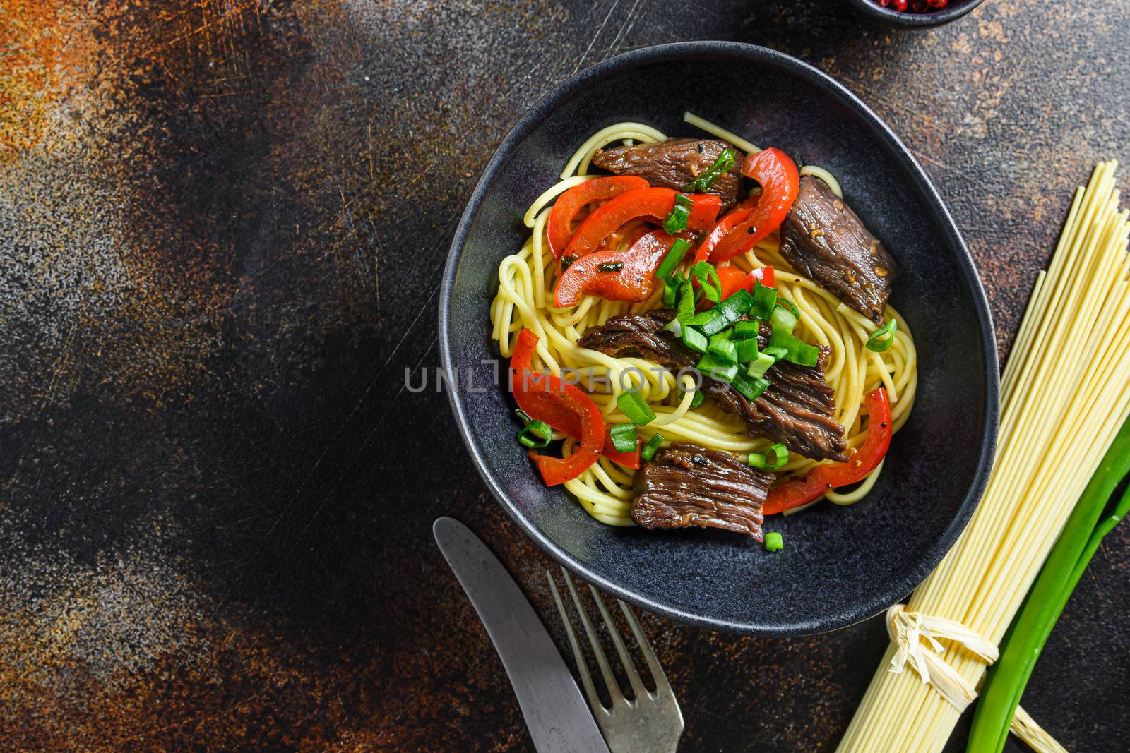 Chinese noodles with vegetables and beef in black bowl top view close up space for text..